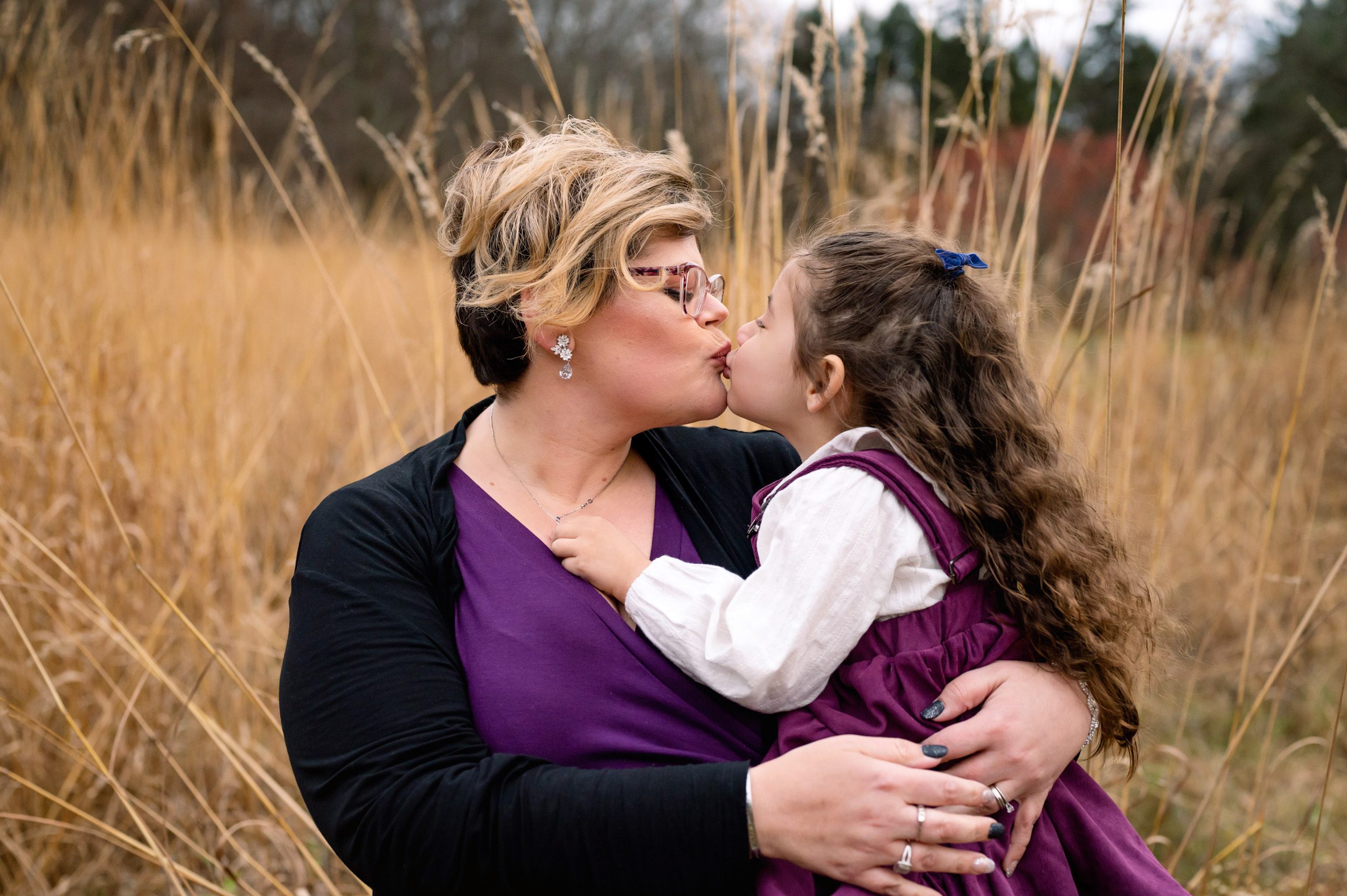 An aunt giving her niece a kiss in a field of golden grasses during an extended family photo session
