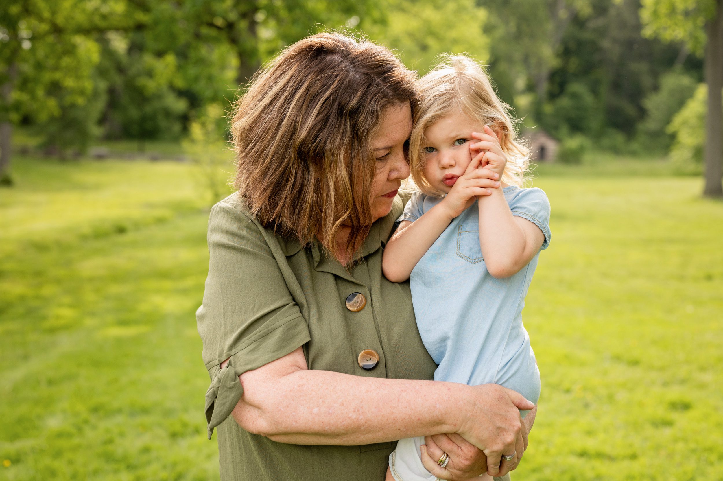 A grandmother snuggling with her granddaughter in a grassy field during an extended family photo session