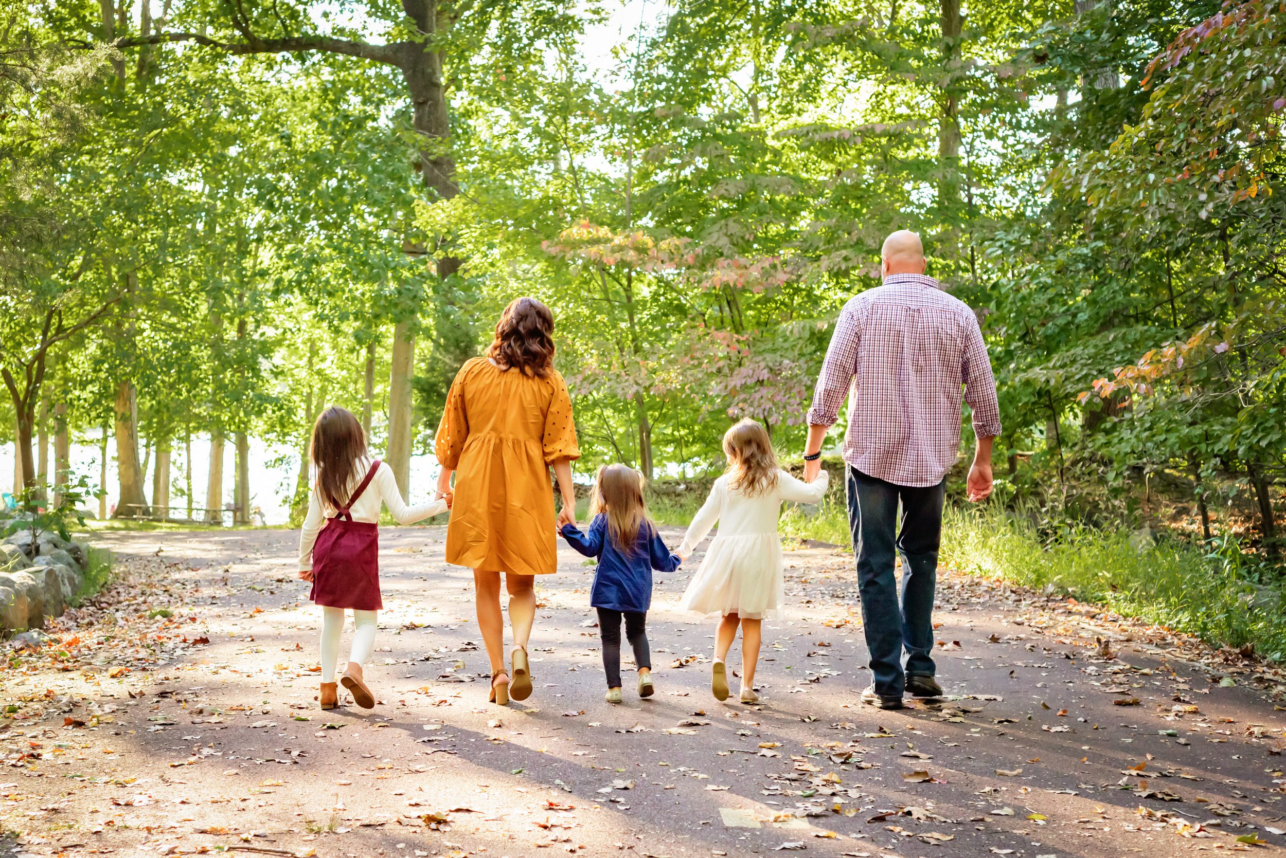 Grandparents holding hands with their three granddaughters and walking away from the camera as the sun shines through the trees during an extended family photo session