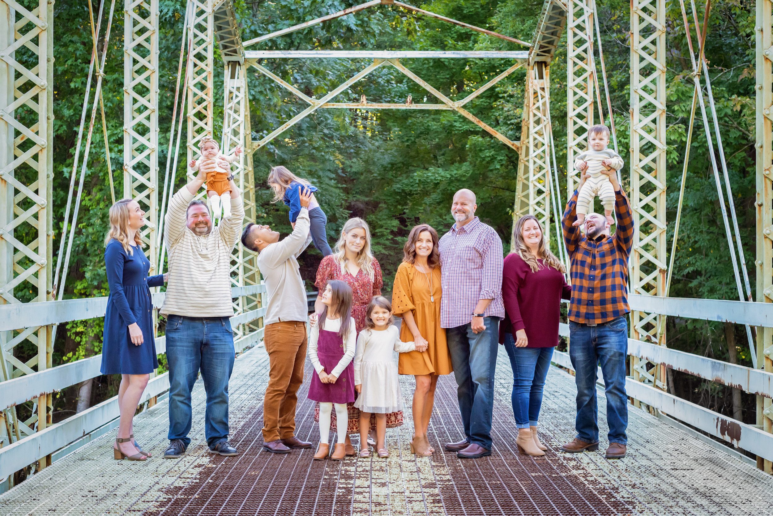 An extended family standing on a bridge and holding the young babies up in the air and laughing during an extended family photo session