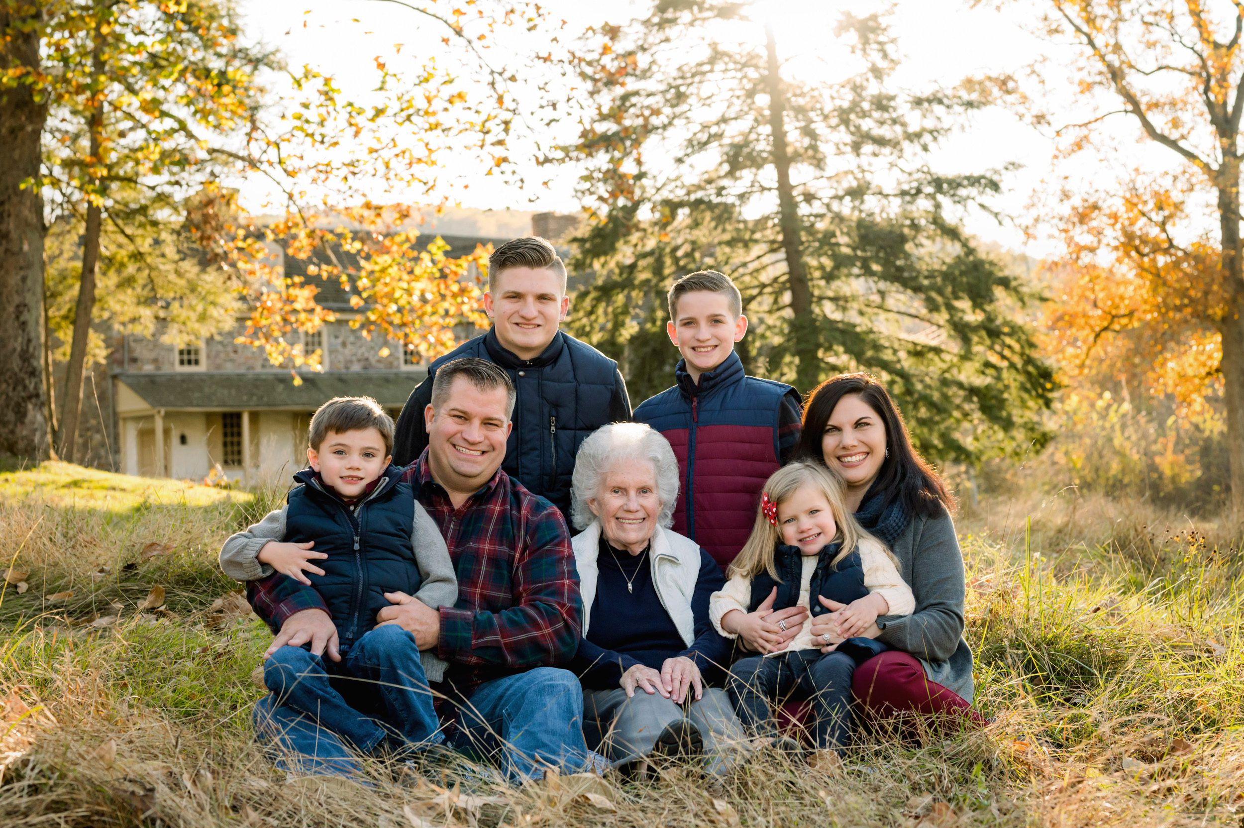 An extended family snuggling together in the grass with the sun shining through the trees in the background during an extended family photo session