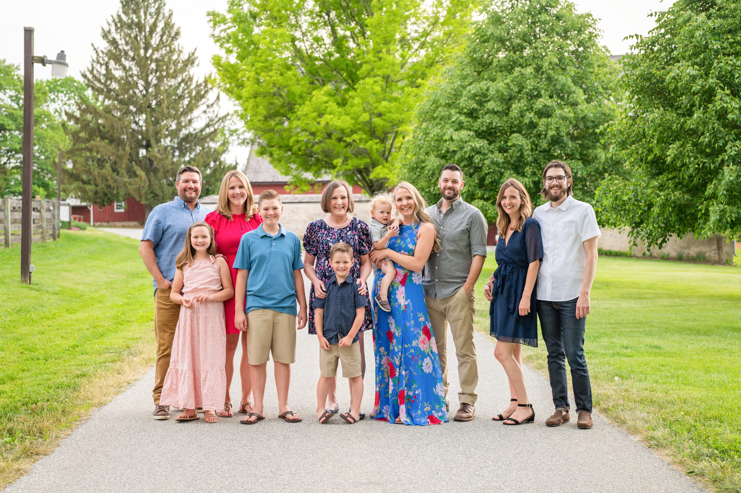 An extended family standing on a pathway with trees and red barns in the background during an extended family photo session