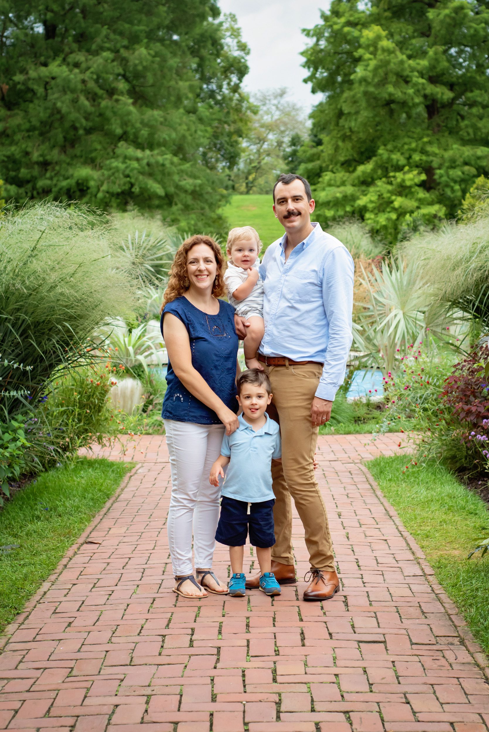 Two young boys and their parents standing on a brick path surrounded by flower gardens during a family photoshoot
