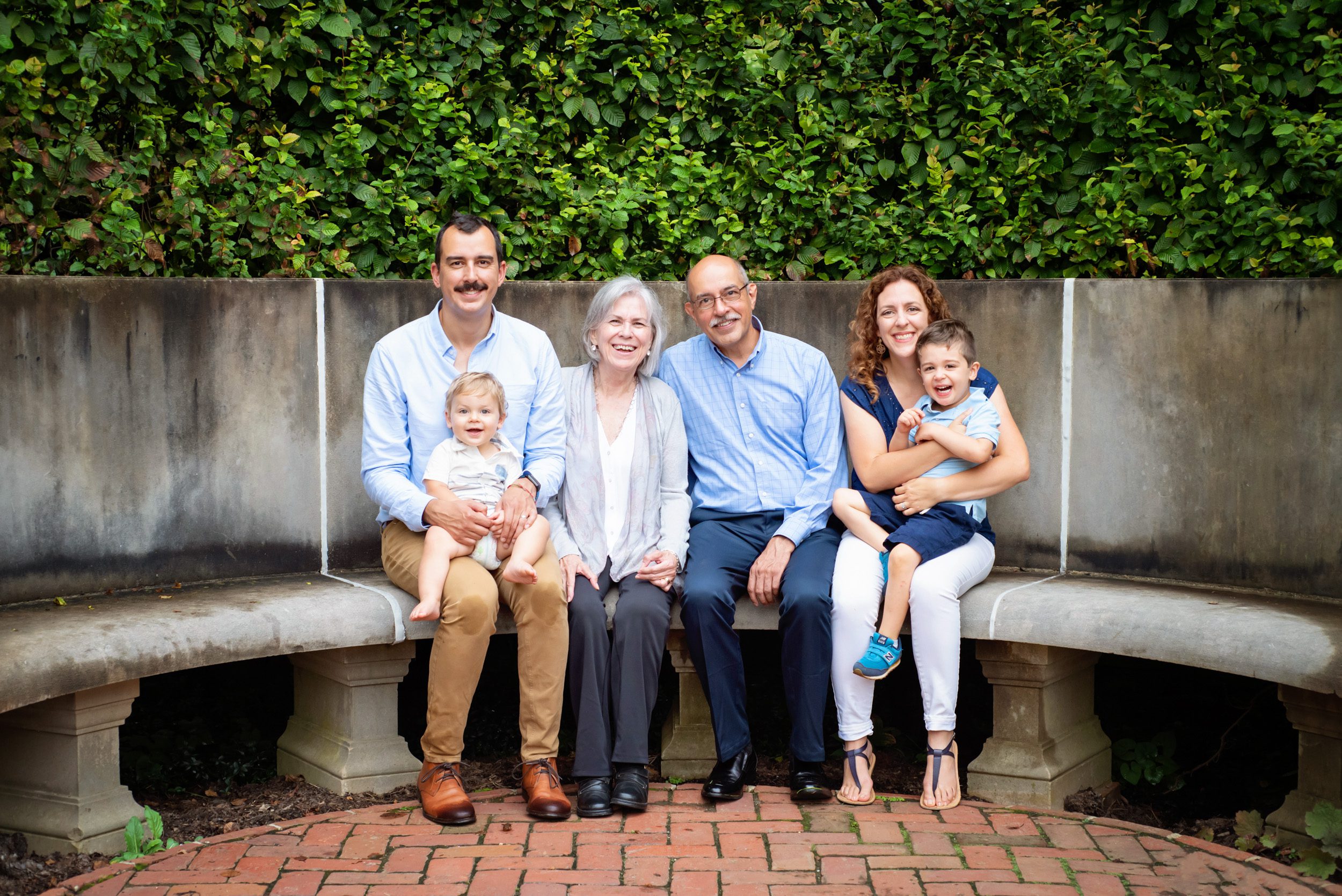Grandparents sitting a bench with their son, daughter-in-law, and two grandsons during an extended family photoshoot