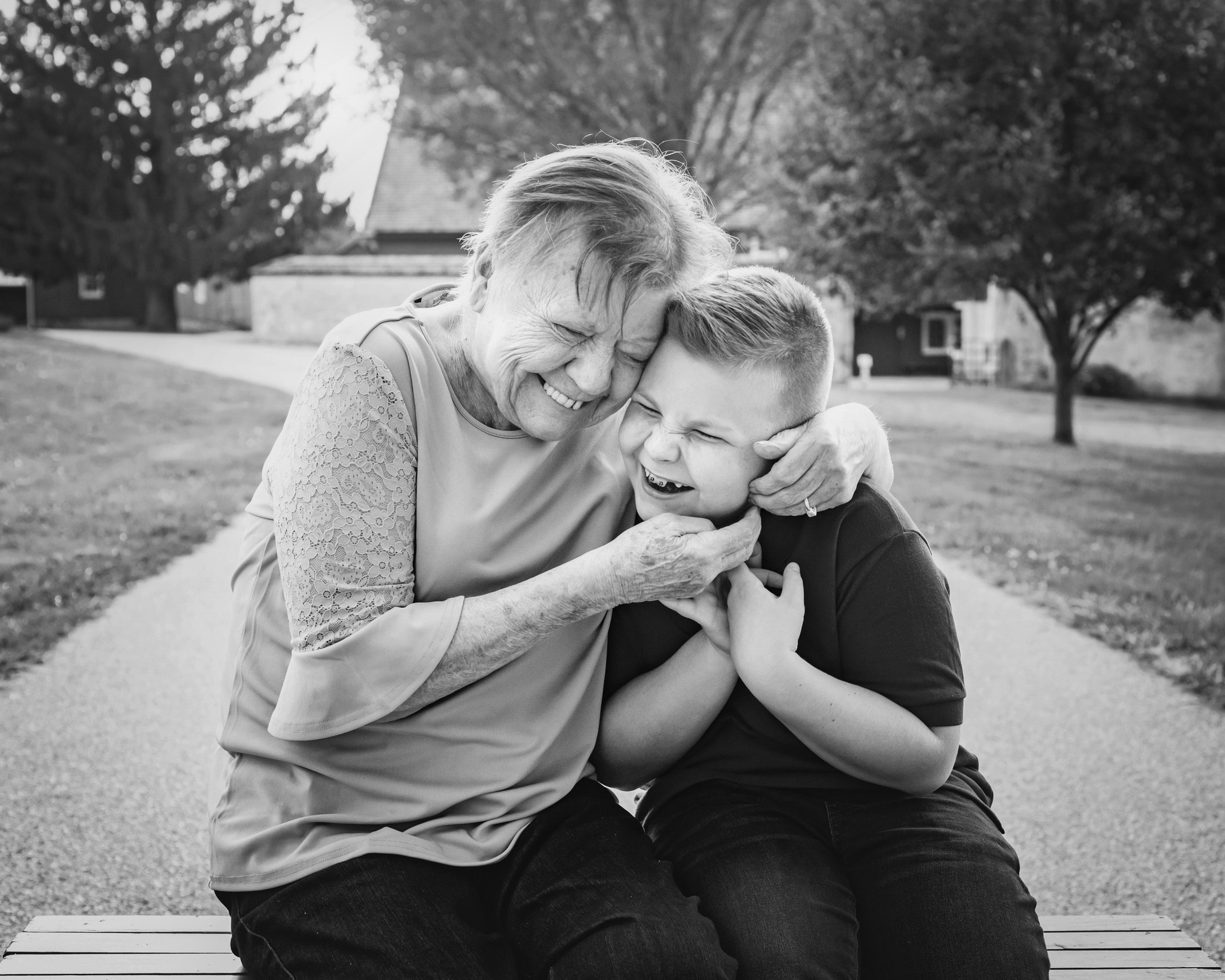 A black and white image of a grandmother hugging her grandson tightly to her cheek as they both laugh during an extended family photo session