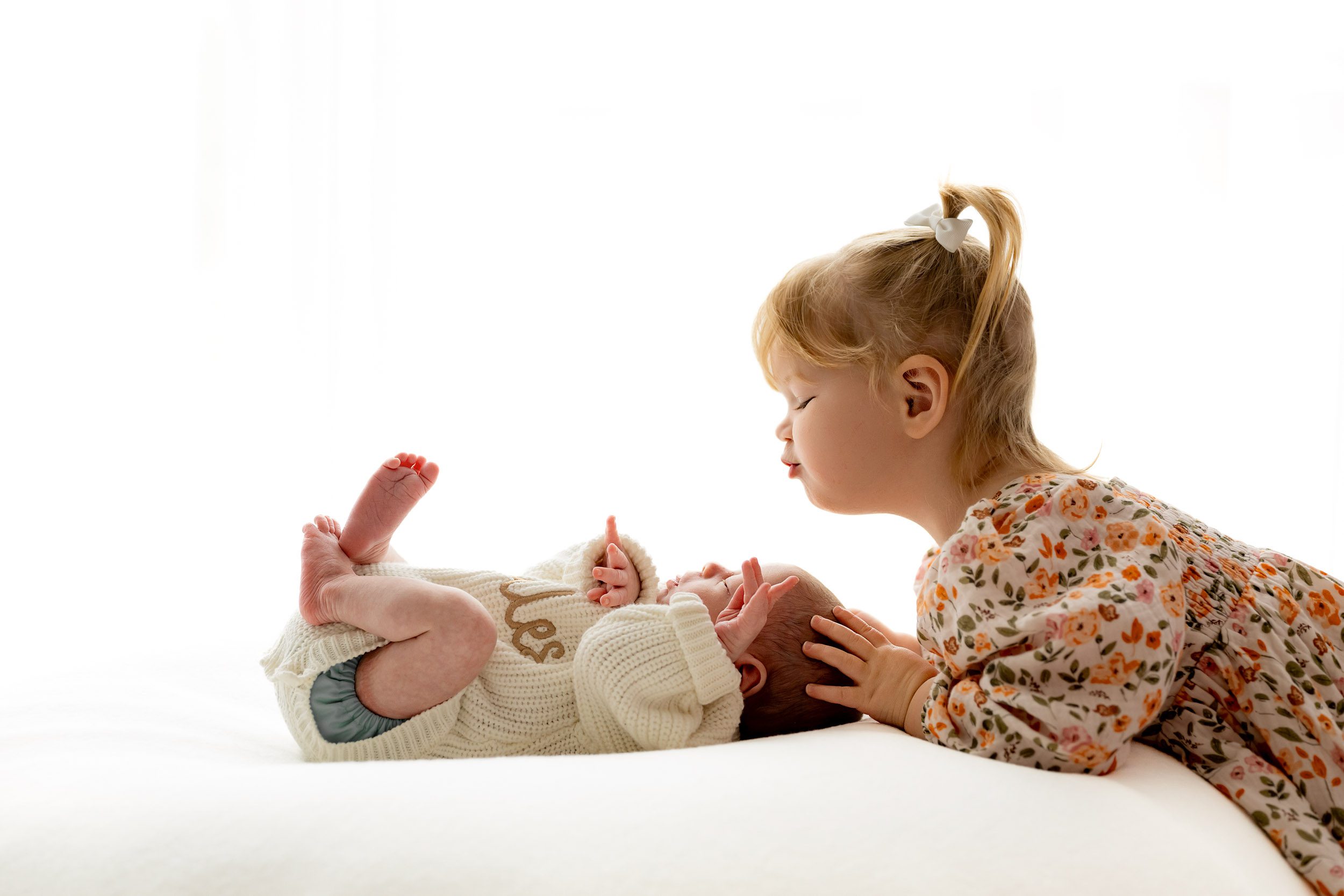 a baby boy laying on a bean bag as his big sister gently touches his head during a newborn photography session