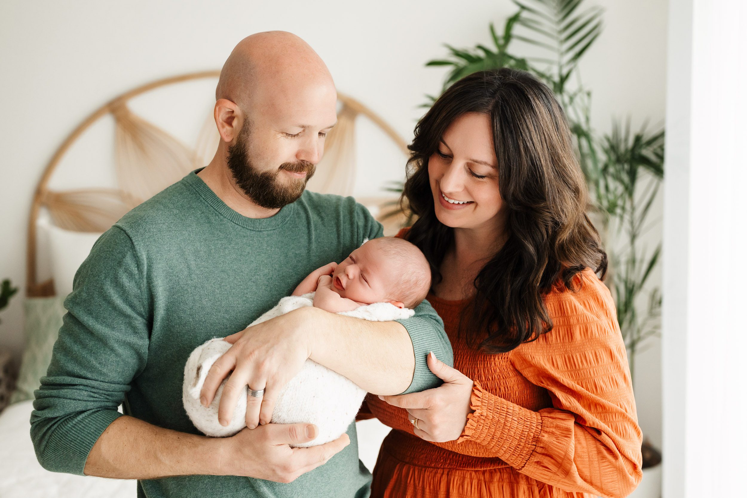 new parents holding their baby boy in their arms and smiling down at him during a newborn photography session