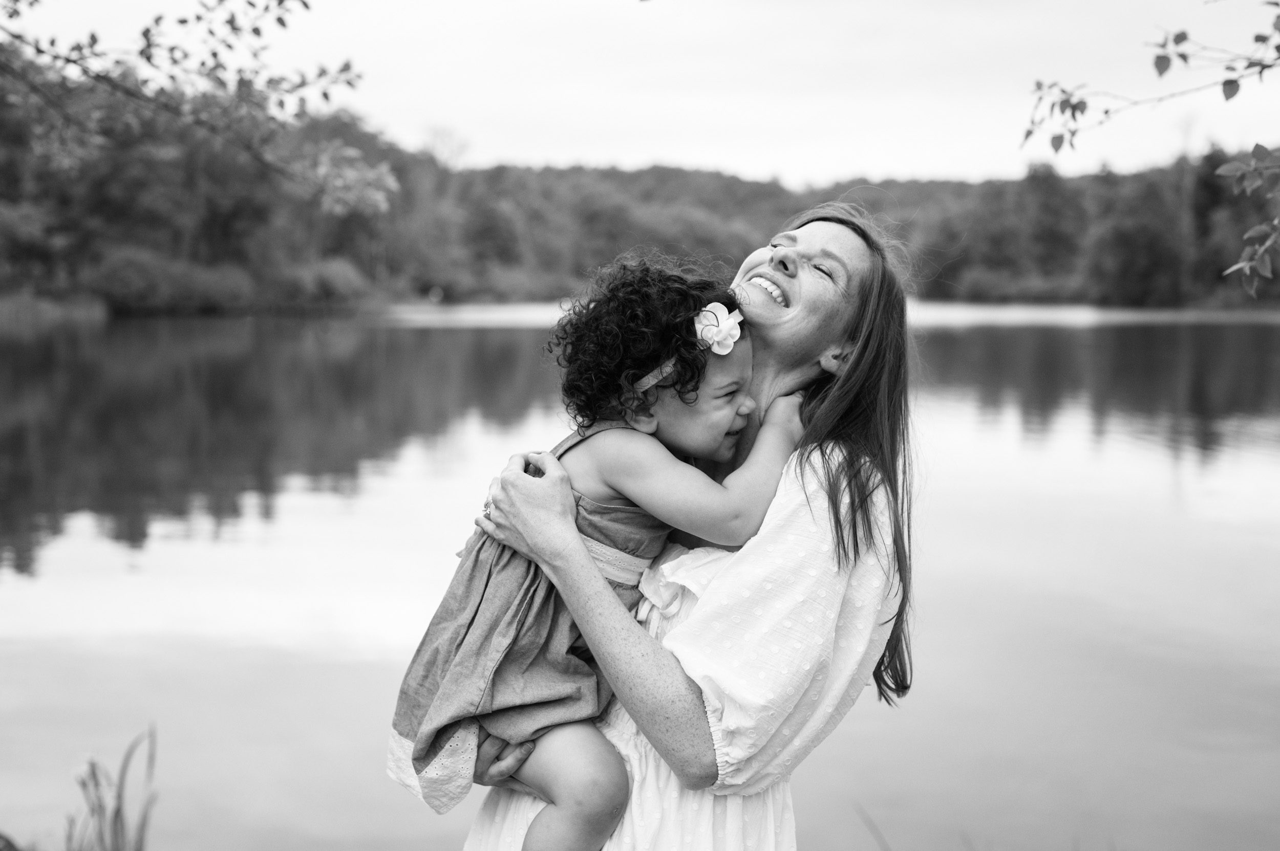 a black and white picture of a young girl blowing raspberries on her mom's neck during a family photo session