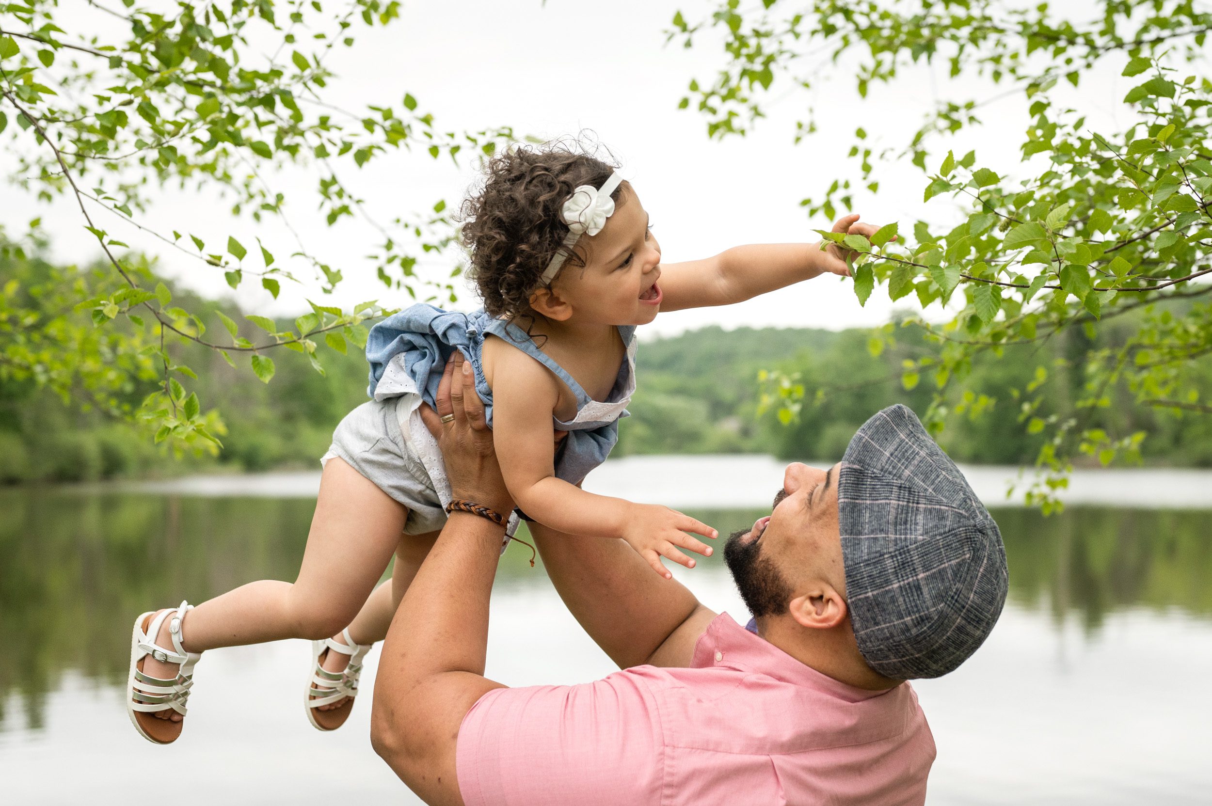 A little girl reaching for a leaf on a tree as her dad flies her through the air during a family photo session