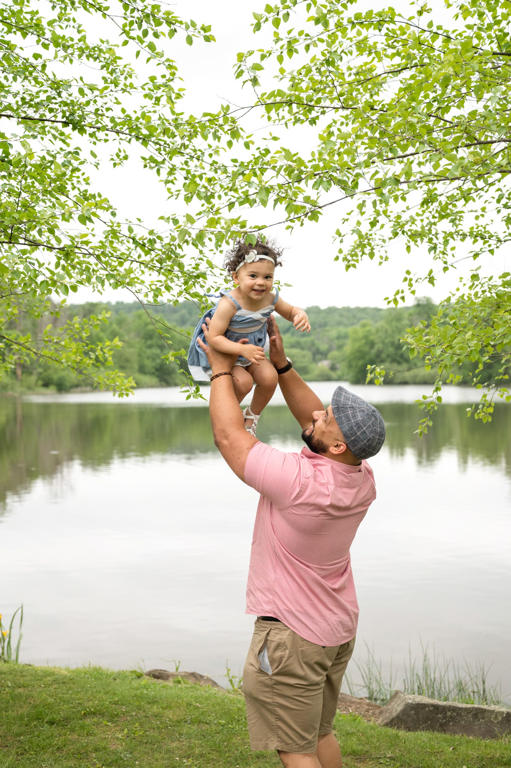 A father flying his young daughter up in the air in front of a lake during a family photoshoot