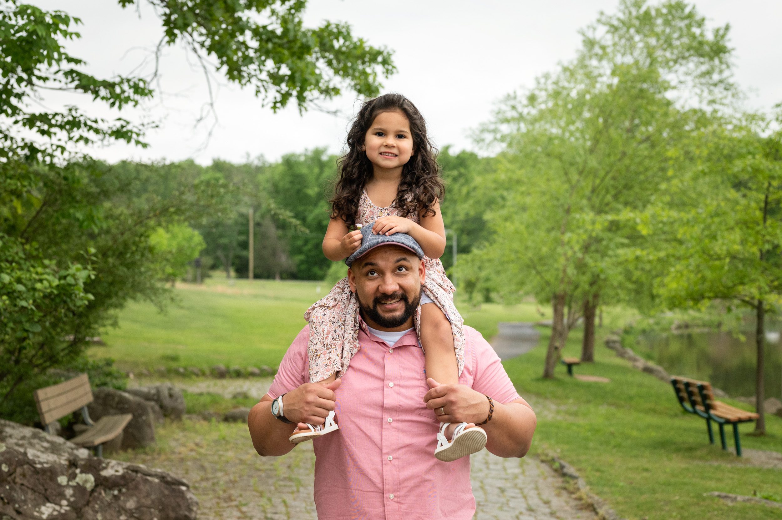 A little girl riding on her father's shoulders as he smiles up at her during a family photo session