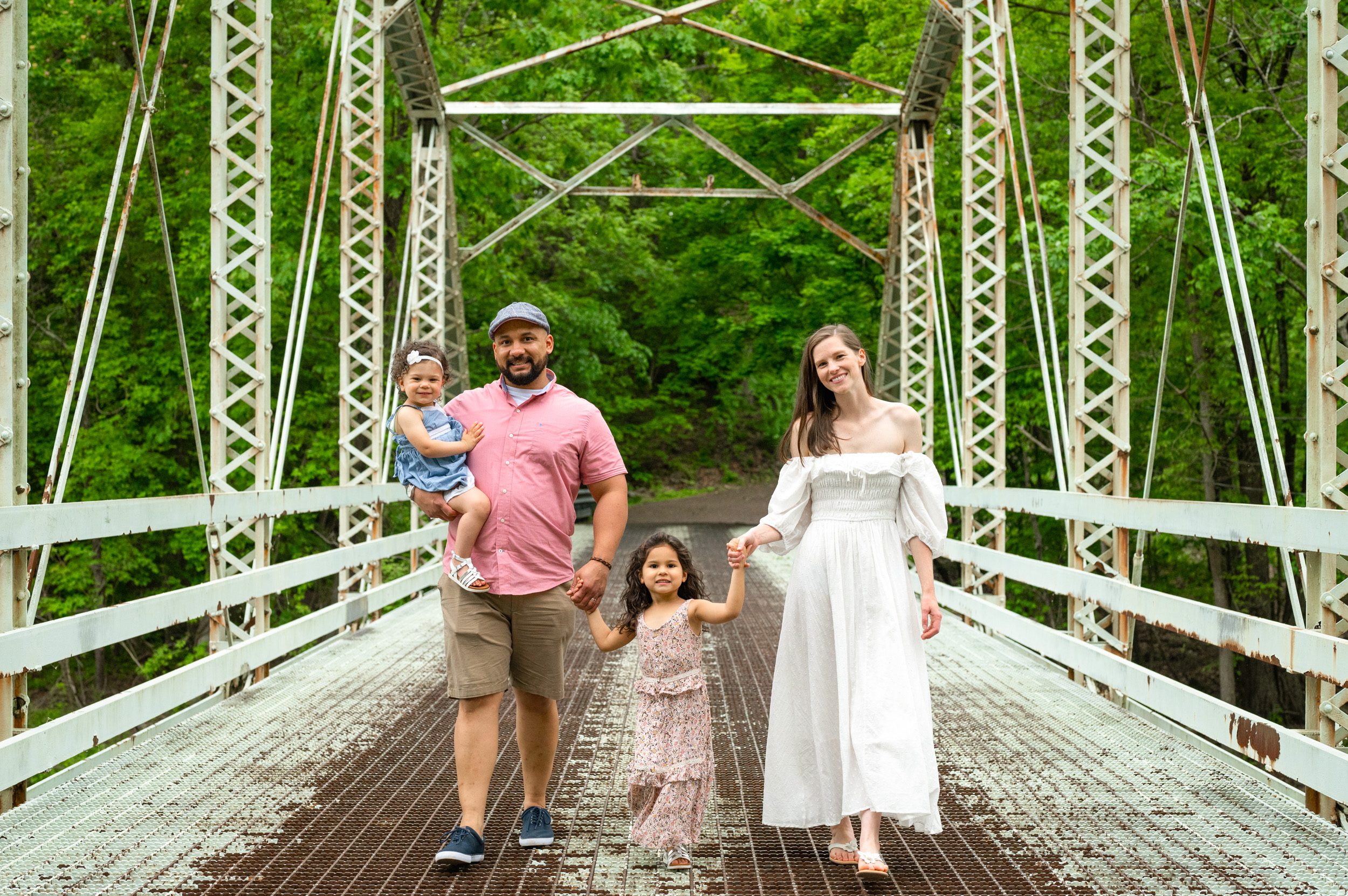 A family of four with two young girls holding hands and walking across a bridge during a pottstown family photo session