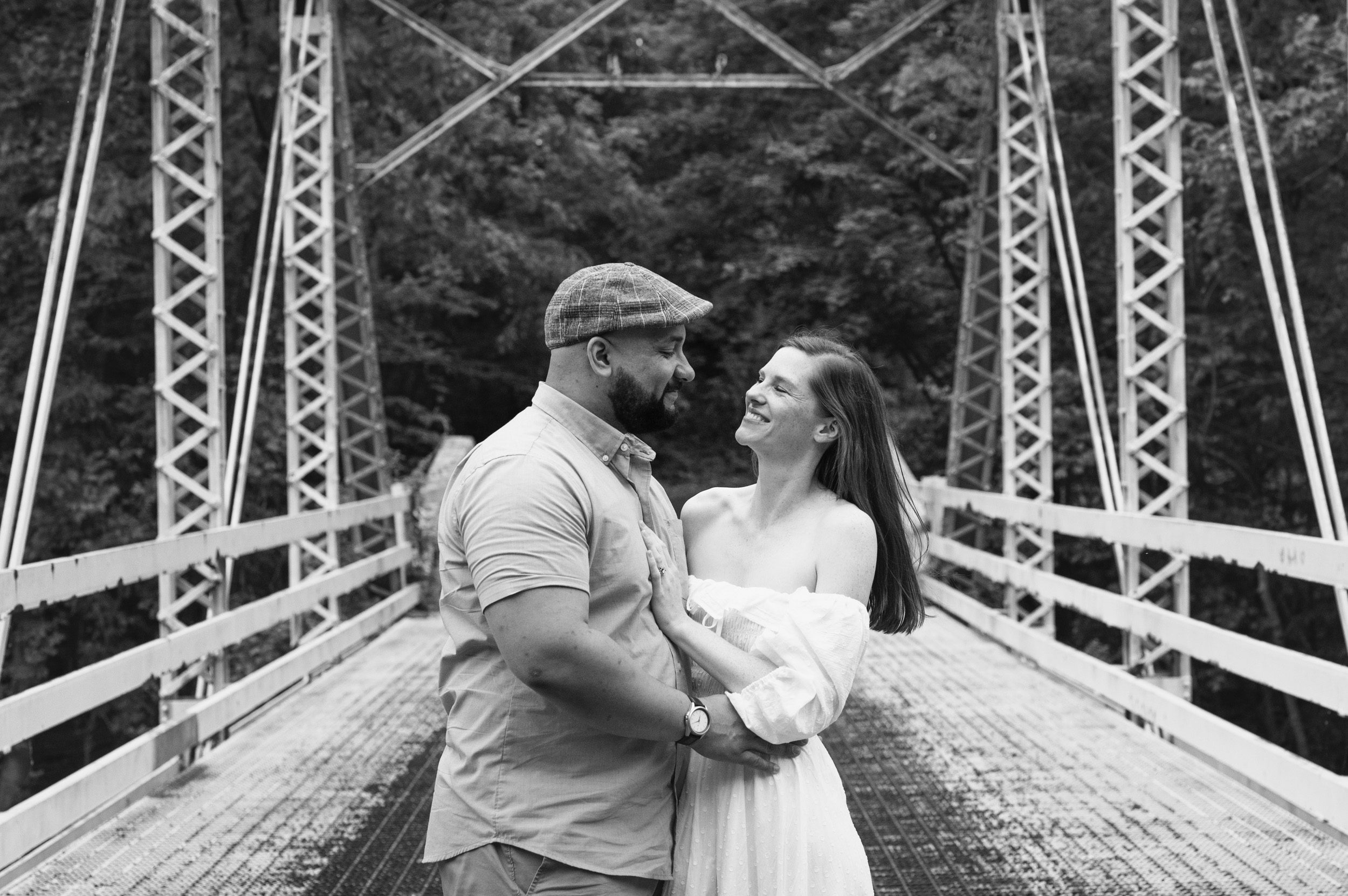 a black and white close up of a couple embracing and smiling at each other on a bridge during a family photoshoot