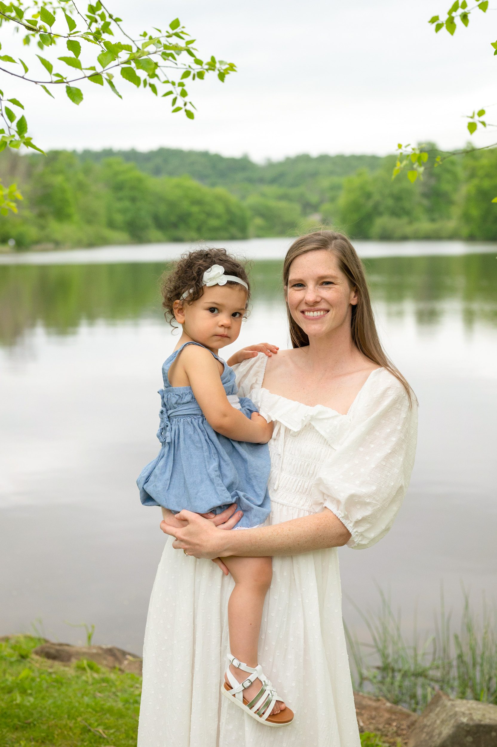 A mom holding her daughter in front of a lake during a family photo session
