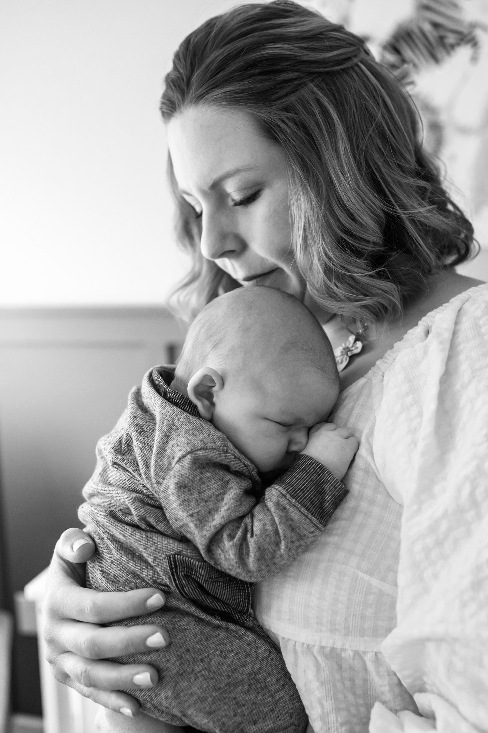black and white image of a new mom snuggling her newborn baby boy against her chest 