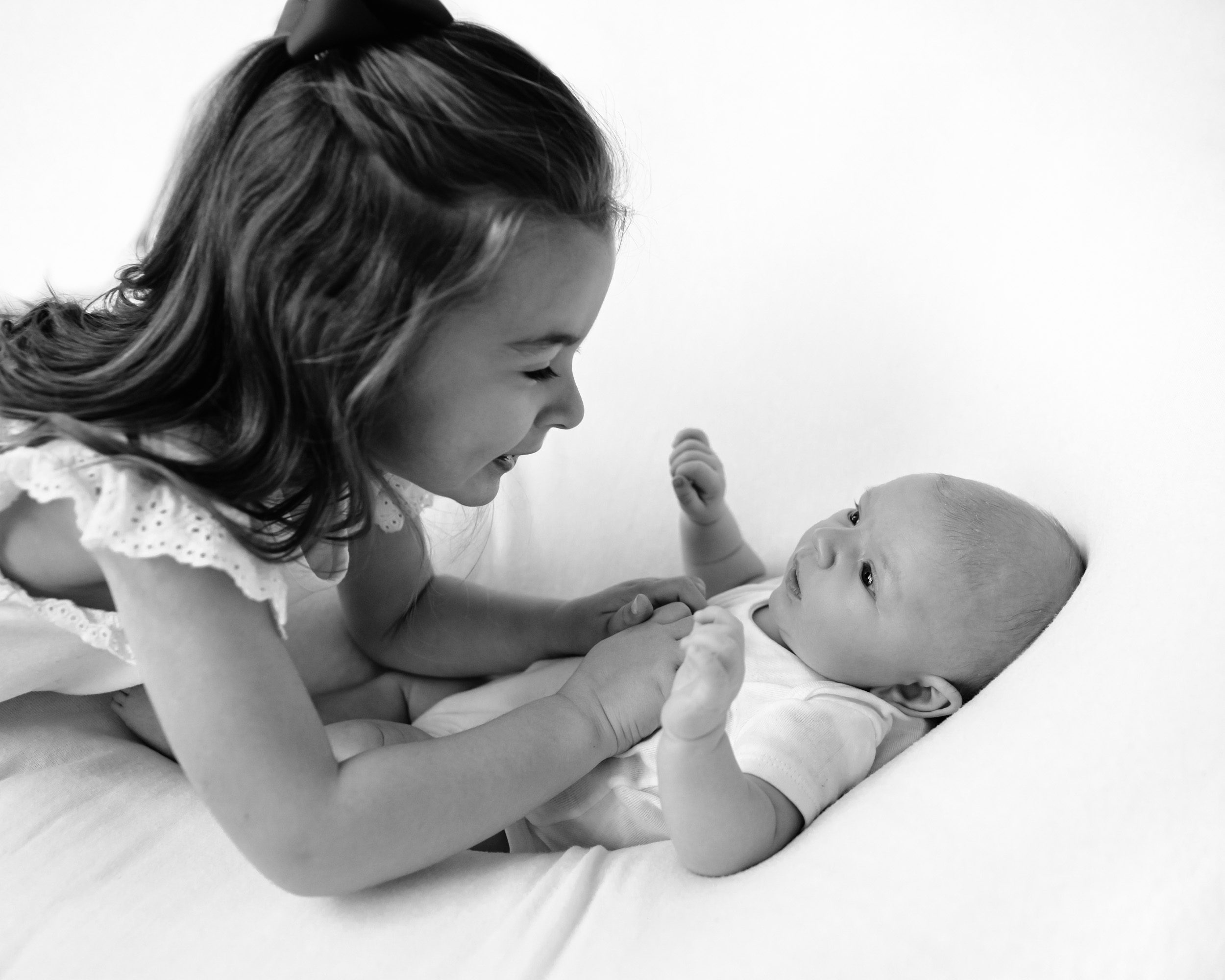 a black and white image of an older sister tickling her new baby brother during a newborn photo session