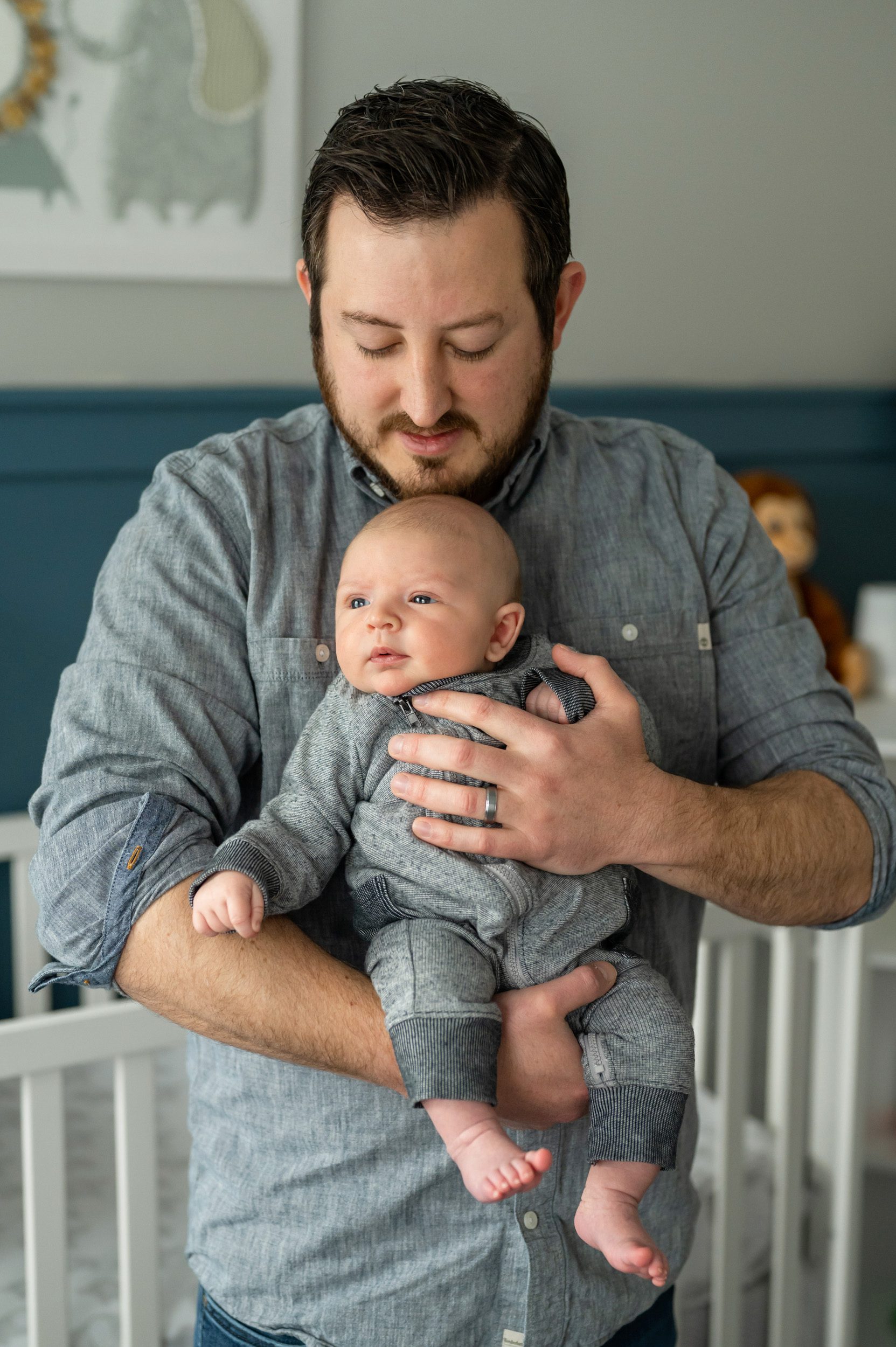 A new father holding his newborn baby boy and smiling down at him during a gilbertsville home newborn photoshoot