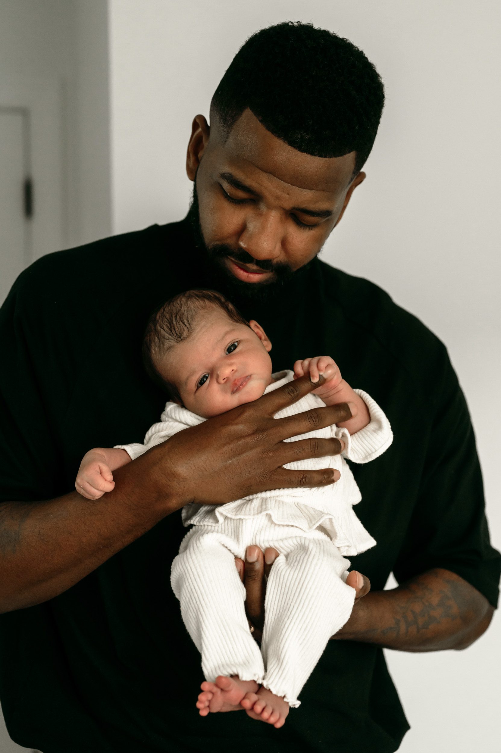 a father holding his newborn baby girl as she grabs onto his finger during a lifestyle newborn photoshoot