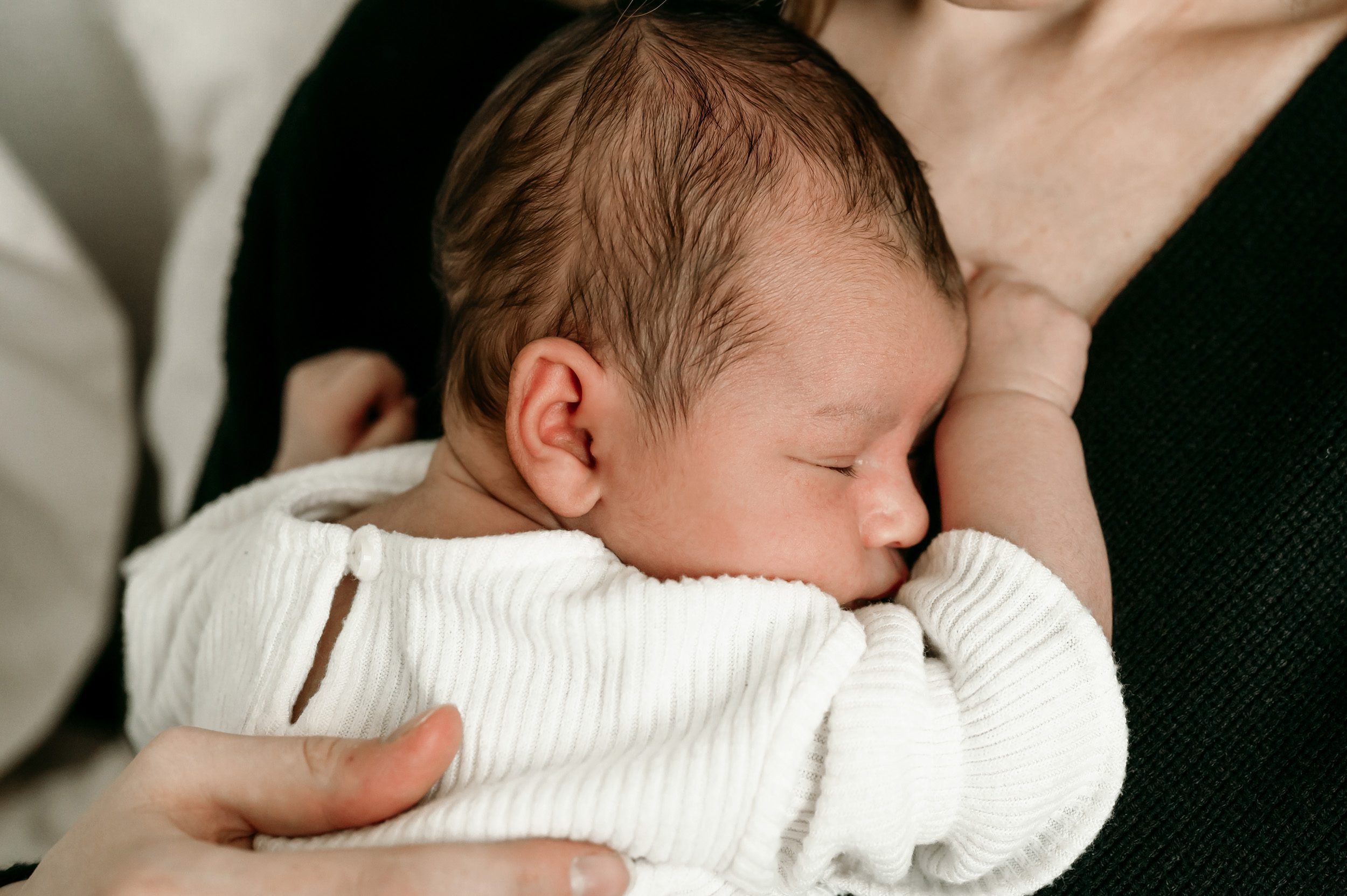 a close up of a newborn baby girl snuggled up against her mom's chest during a lifestyle newborn photo session