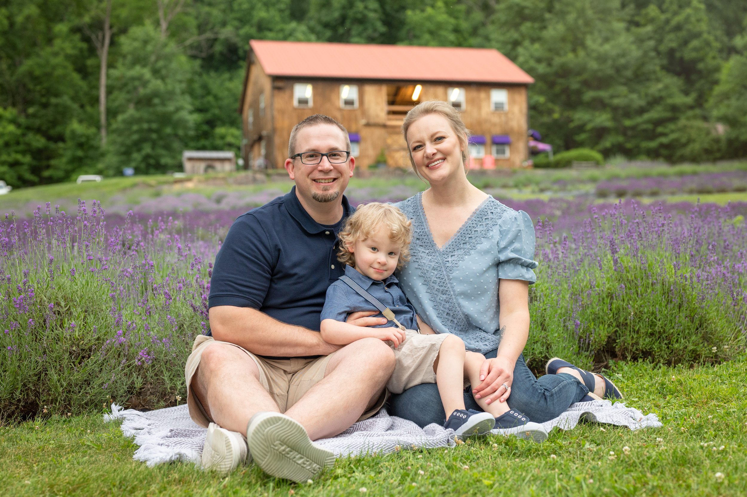 parents sitting in front of a field of purple lavender in bloom with their little boy on their lap during a family photoshoot