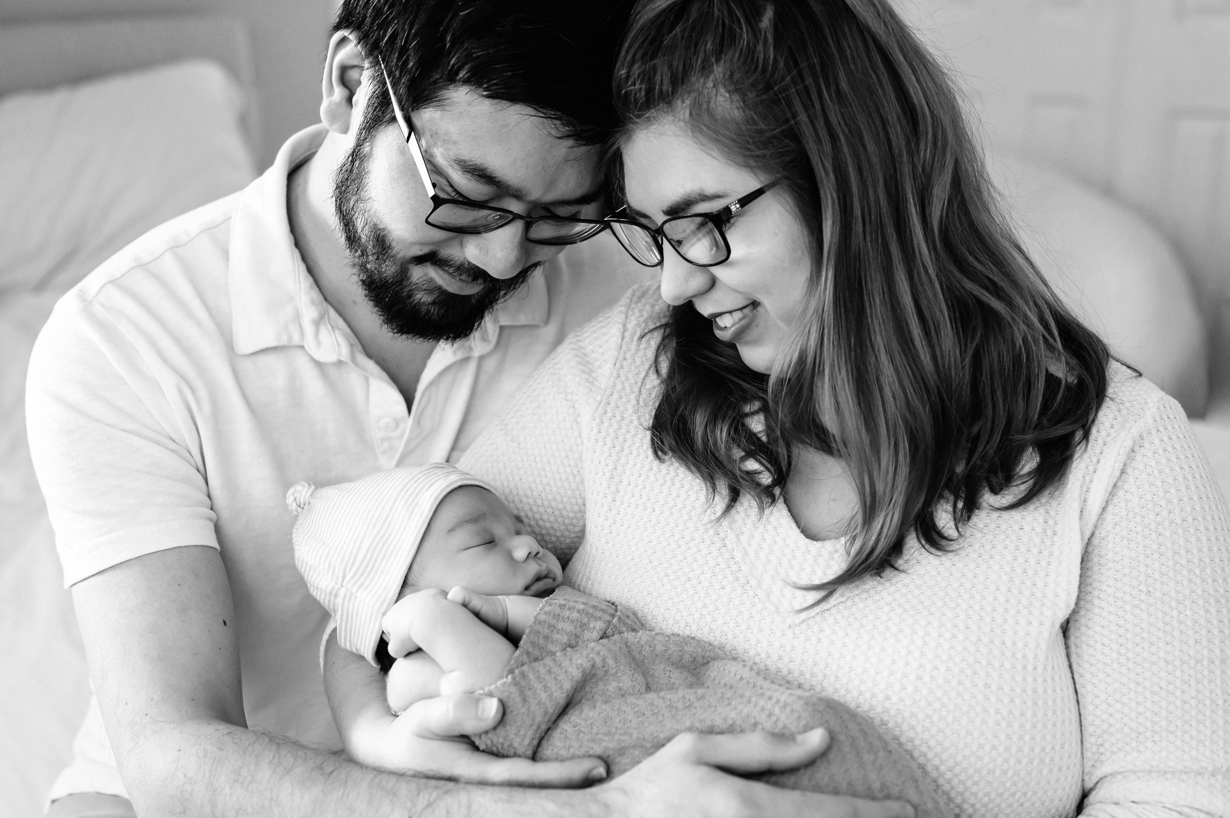 black and white picture of new parents holding their newborn baby boy and smiling down at him during a home newborn photoshoot