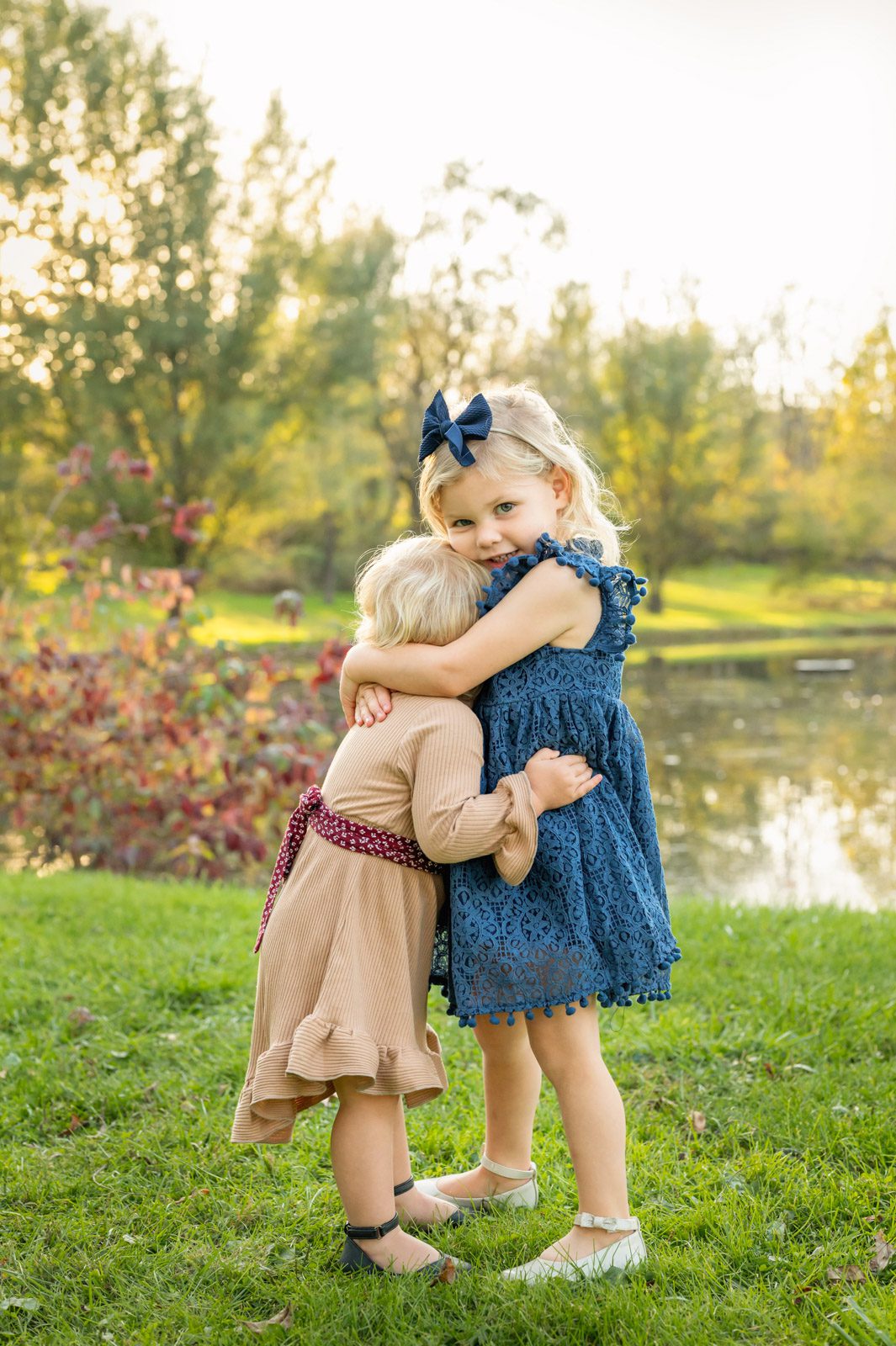 Two young sisters hugging each other in front of a pond during a family photoshoot