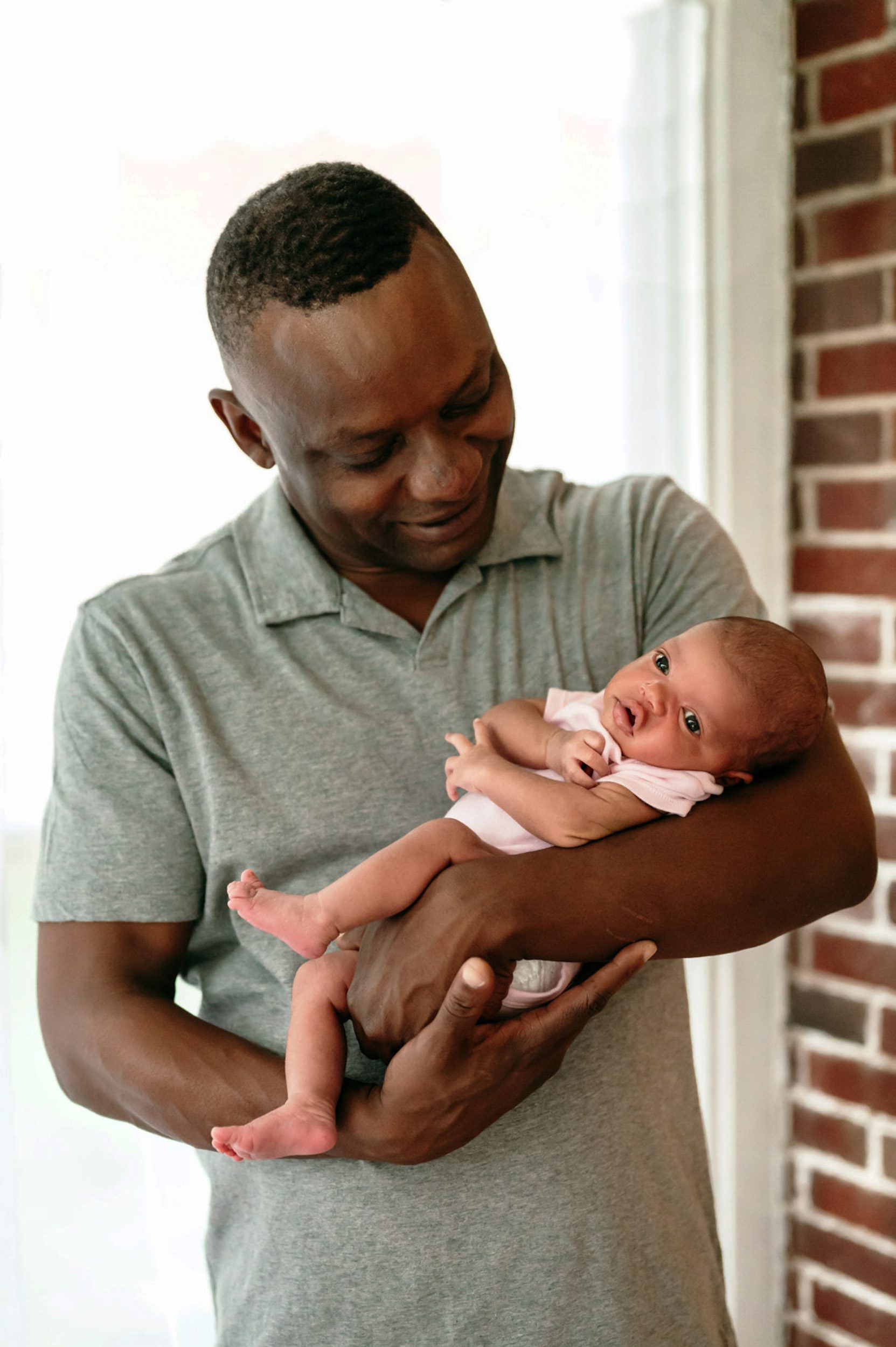 a baby girl cradled in her dad's arms as he smiles down at her during a lifestyle newborn photoshoot