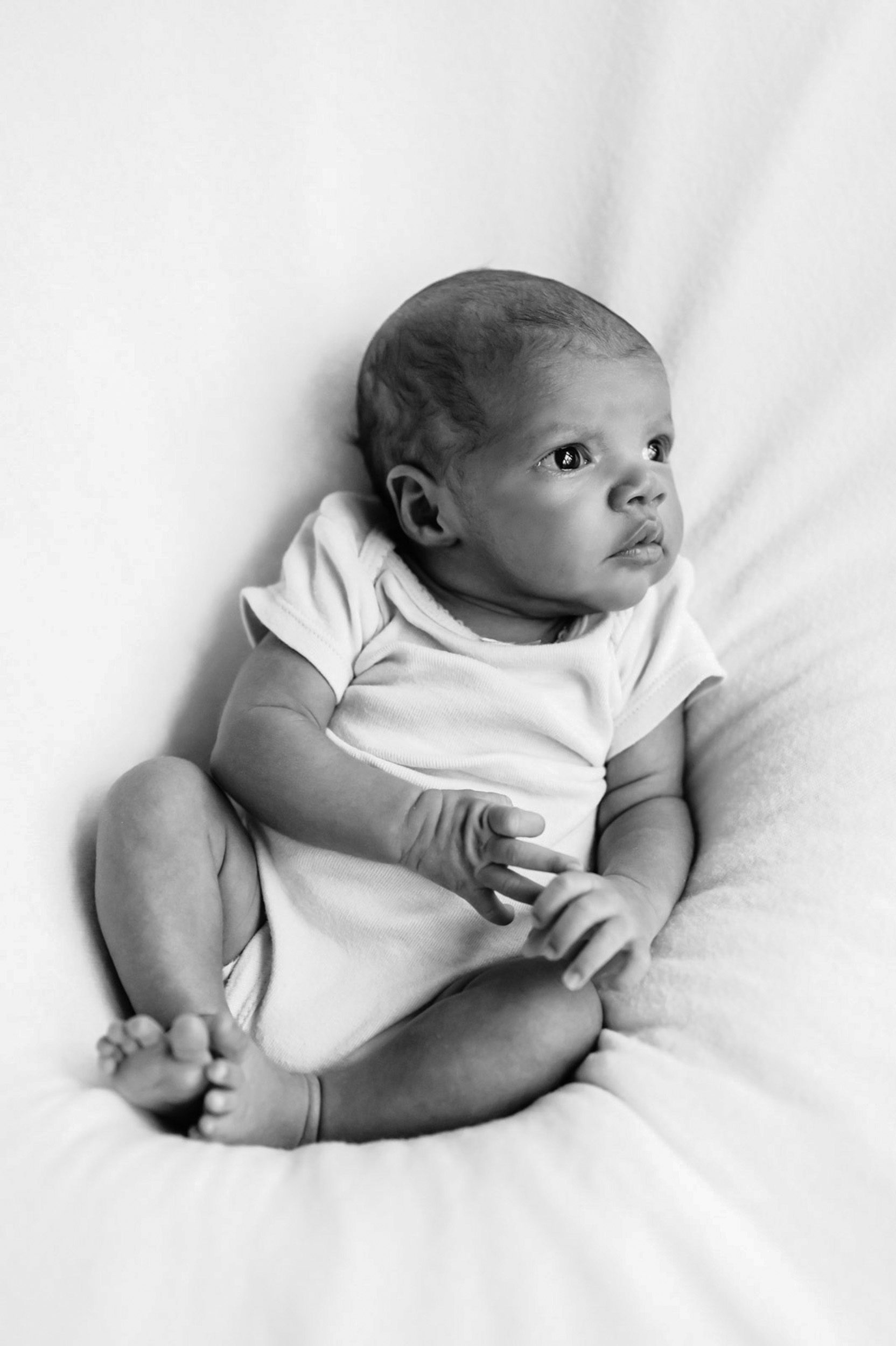 a black and white picture of a baby girl looking off toward the window light during a natural light newborn photoshoot