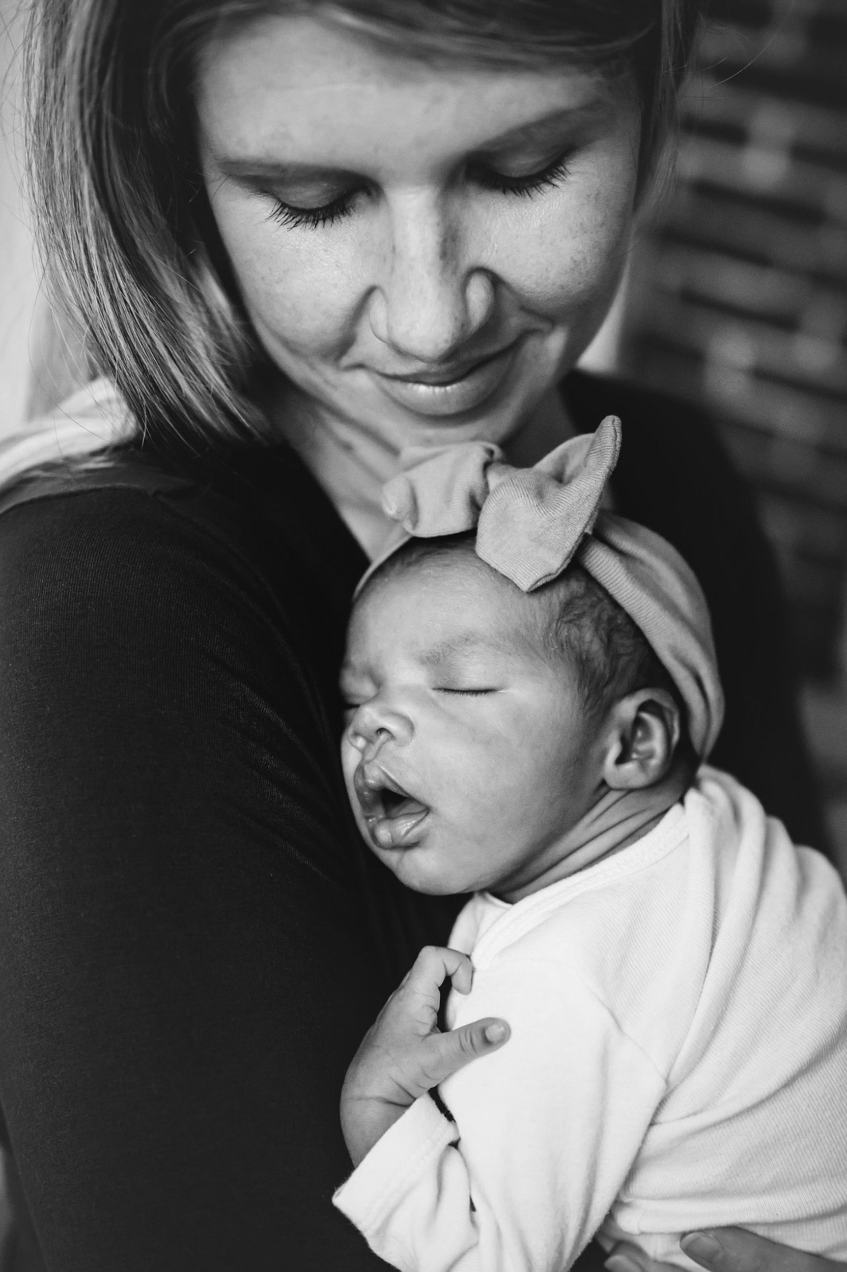 a black and white picture of a baby girl snuggled up against her mom's chest as her mom smiles down at her during a lifestyle newborn photoshoot
