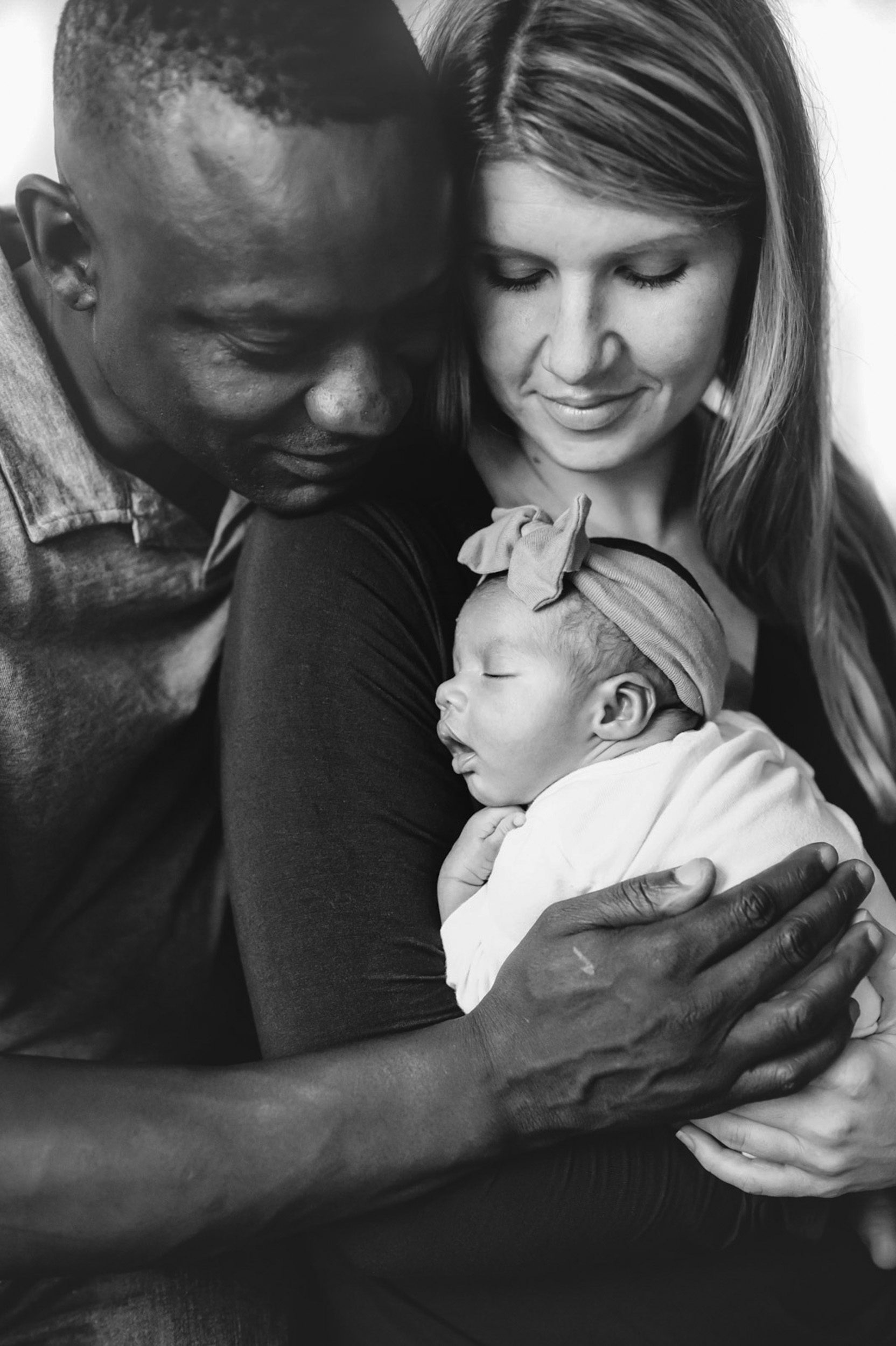 a black and white picture of parents holding their newborn baby girl and smiling at her during a lifestyle newborn photoshoot