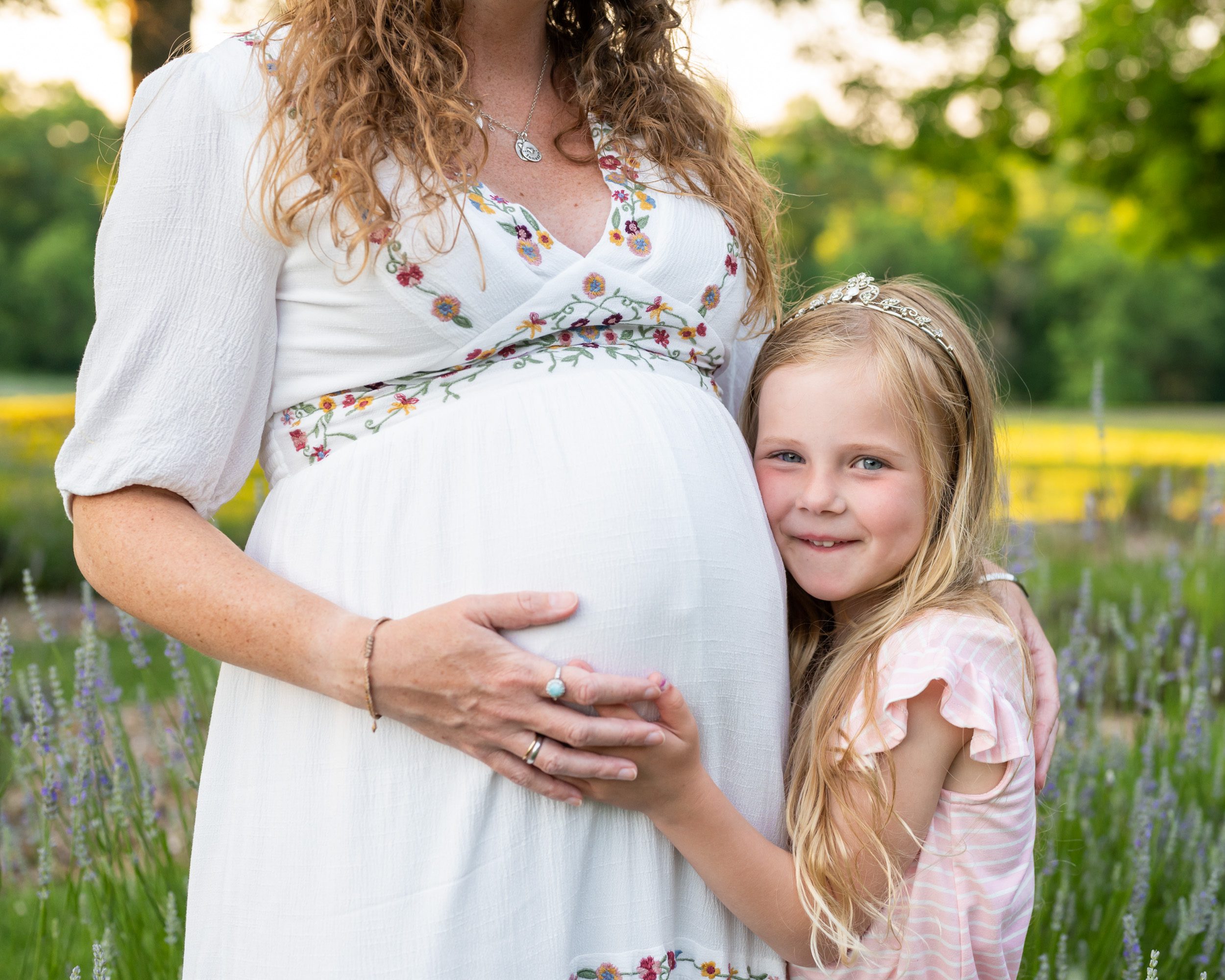 a close up of a girl hugging her expecting mom's belly and smiling at the camera during a maternity photoshoot