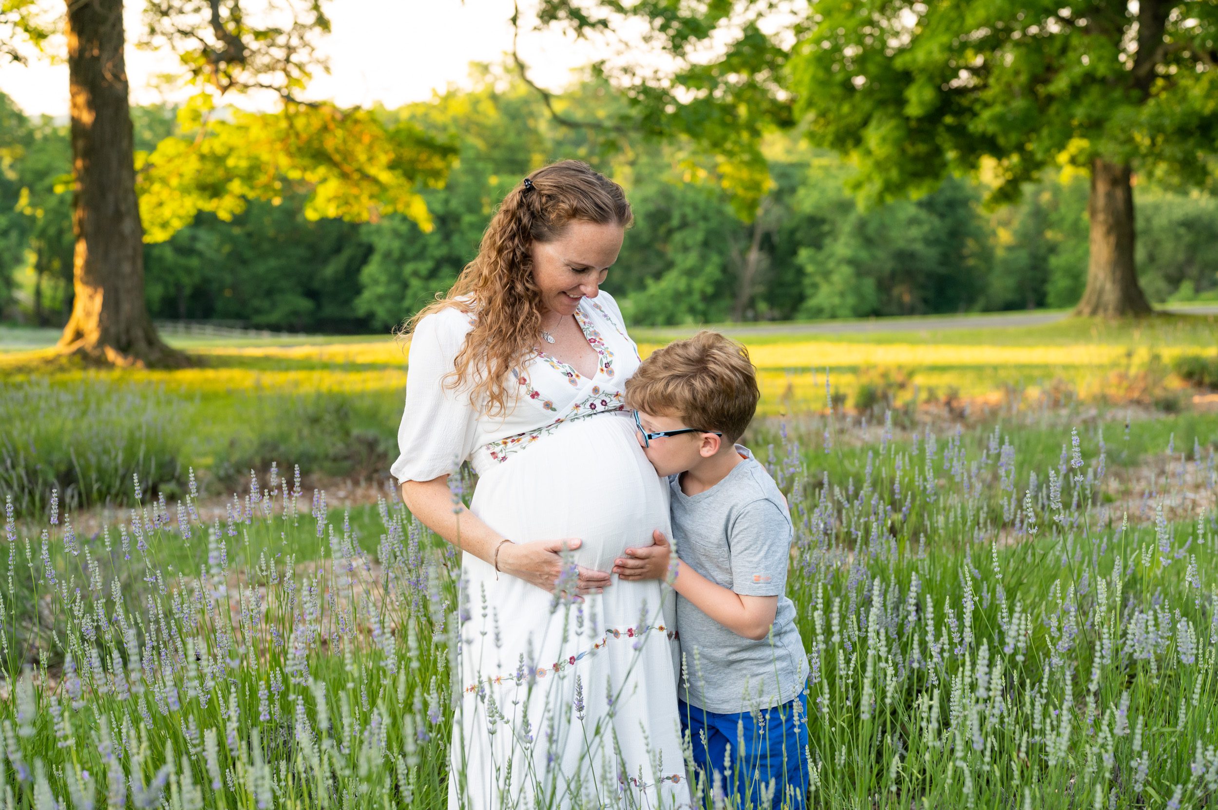 a boy kissing his pregnant mom's belly in a lavender field during a maternity photo session