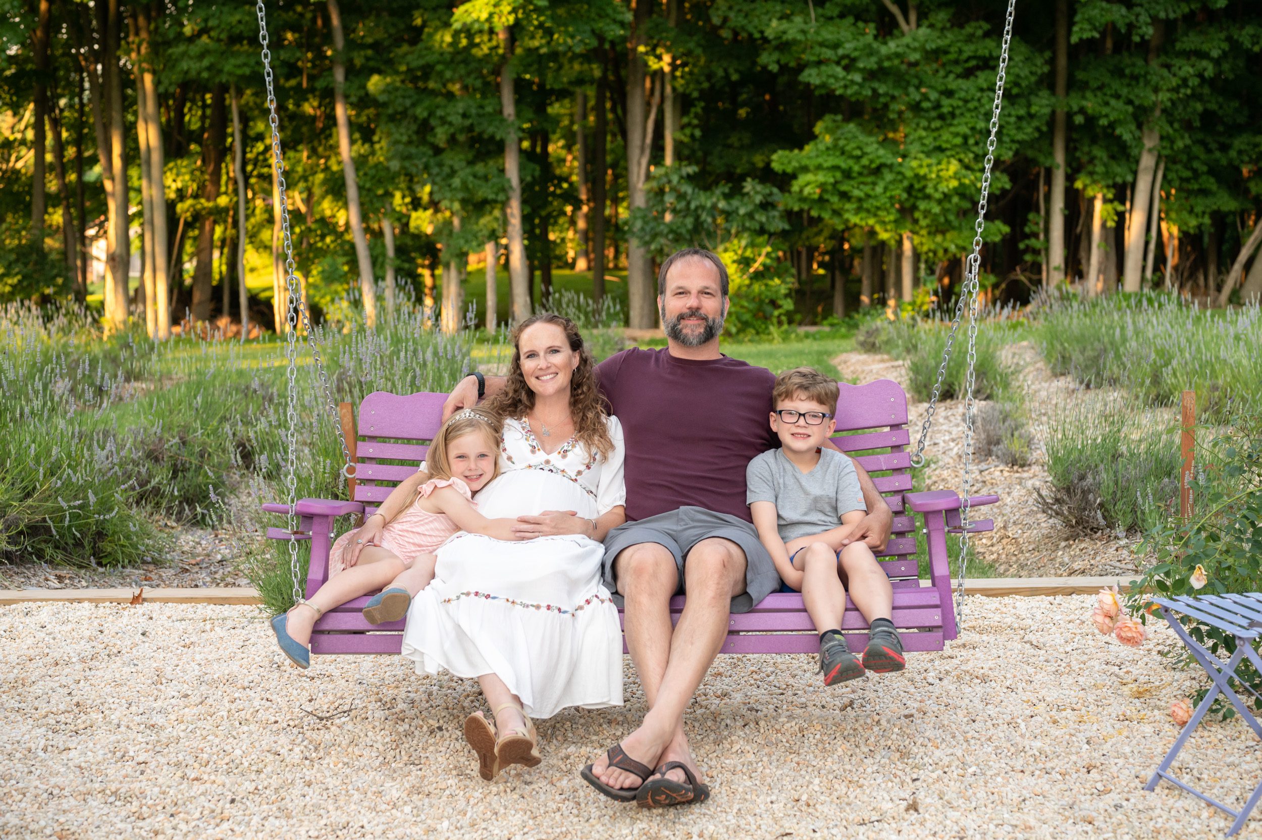 a family of four sitting on a purple swing and smiling at the camera during a maternity photoshoot