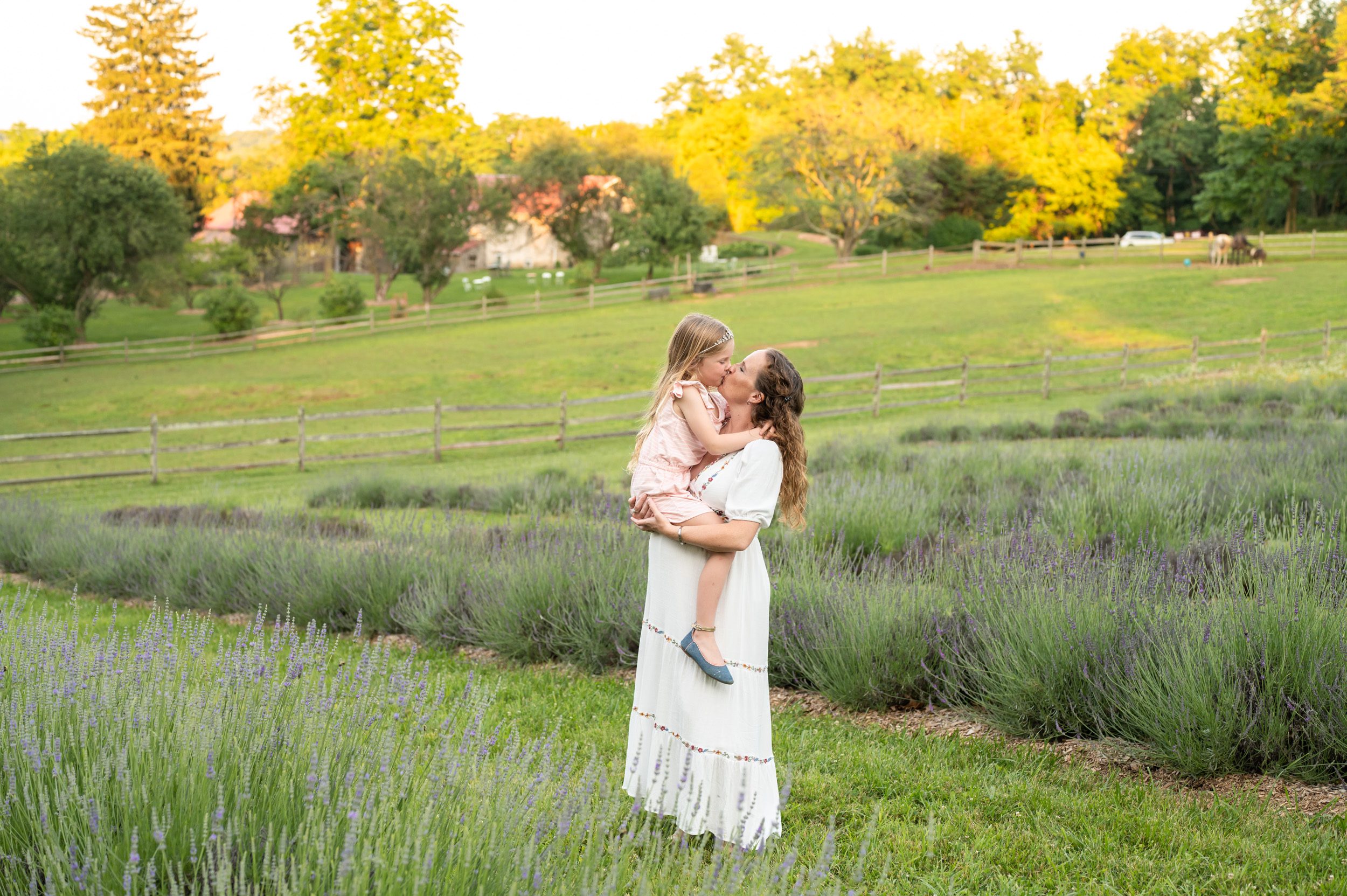 a pregnant mom and her daughter kissing each other in a lavender field during a maternity photo session