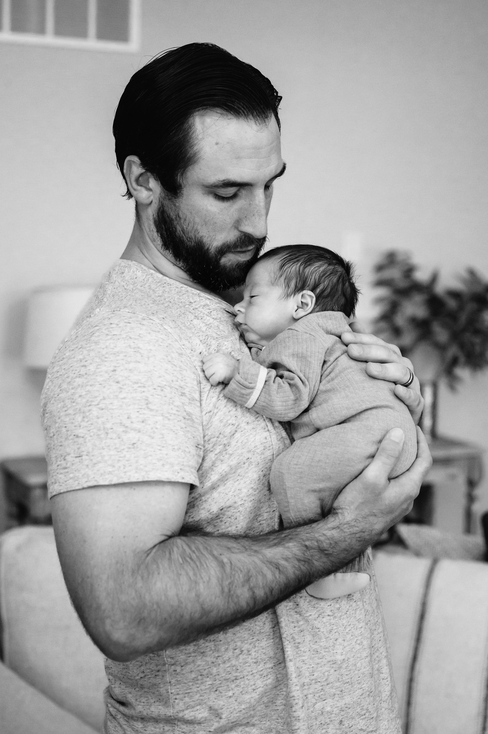 a black and white picture of a newborn baby boy snuggled up against his dad's chest during a newborn photo session