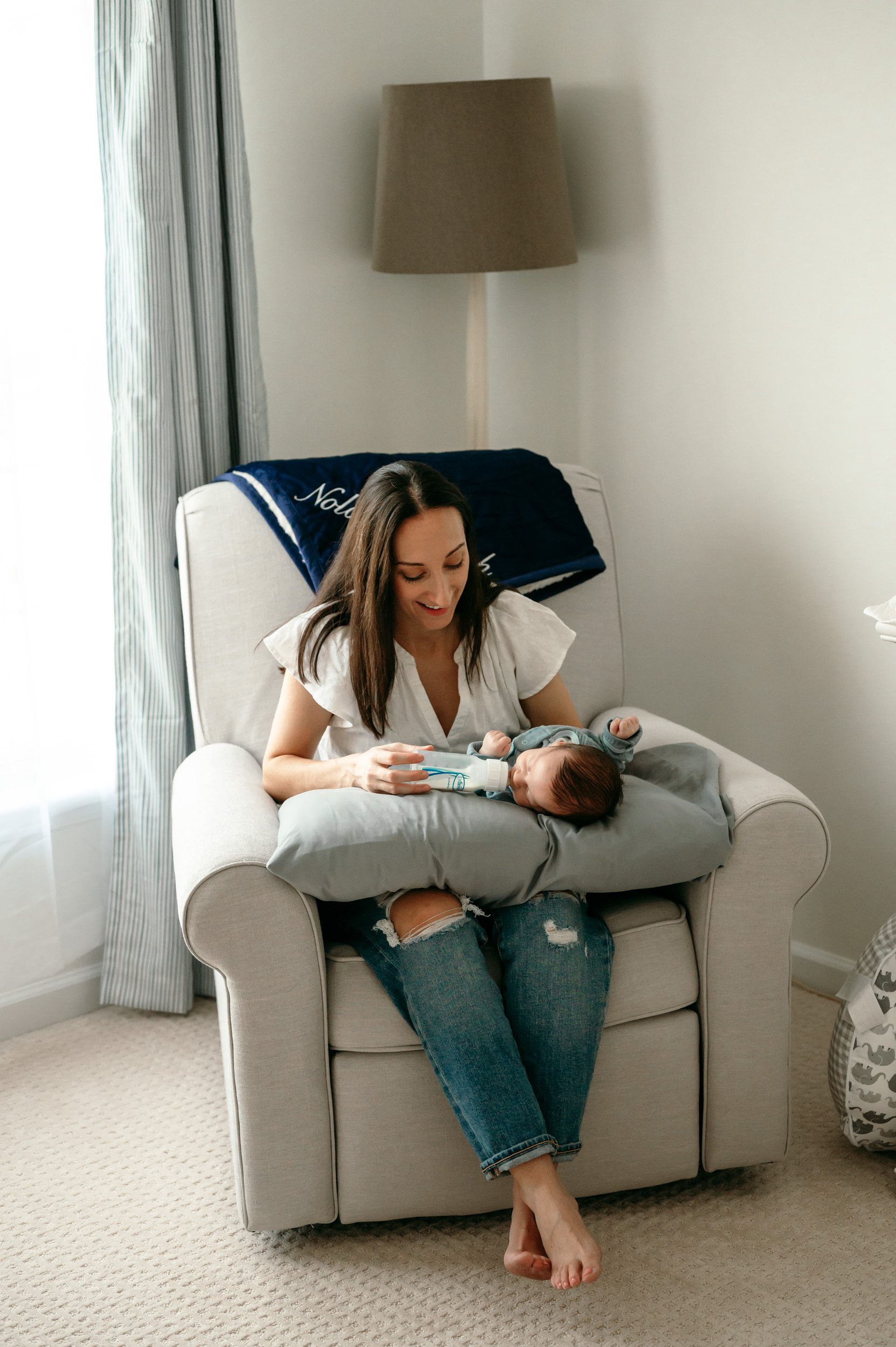 a new mom sitting a rocking chair and feeding her son a bottle during an in home newborn photoshoot