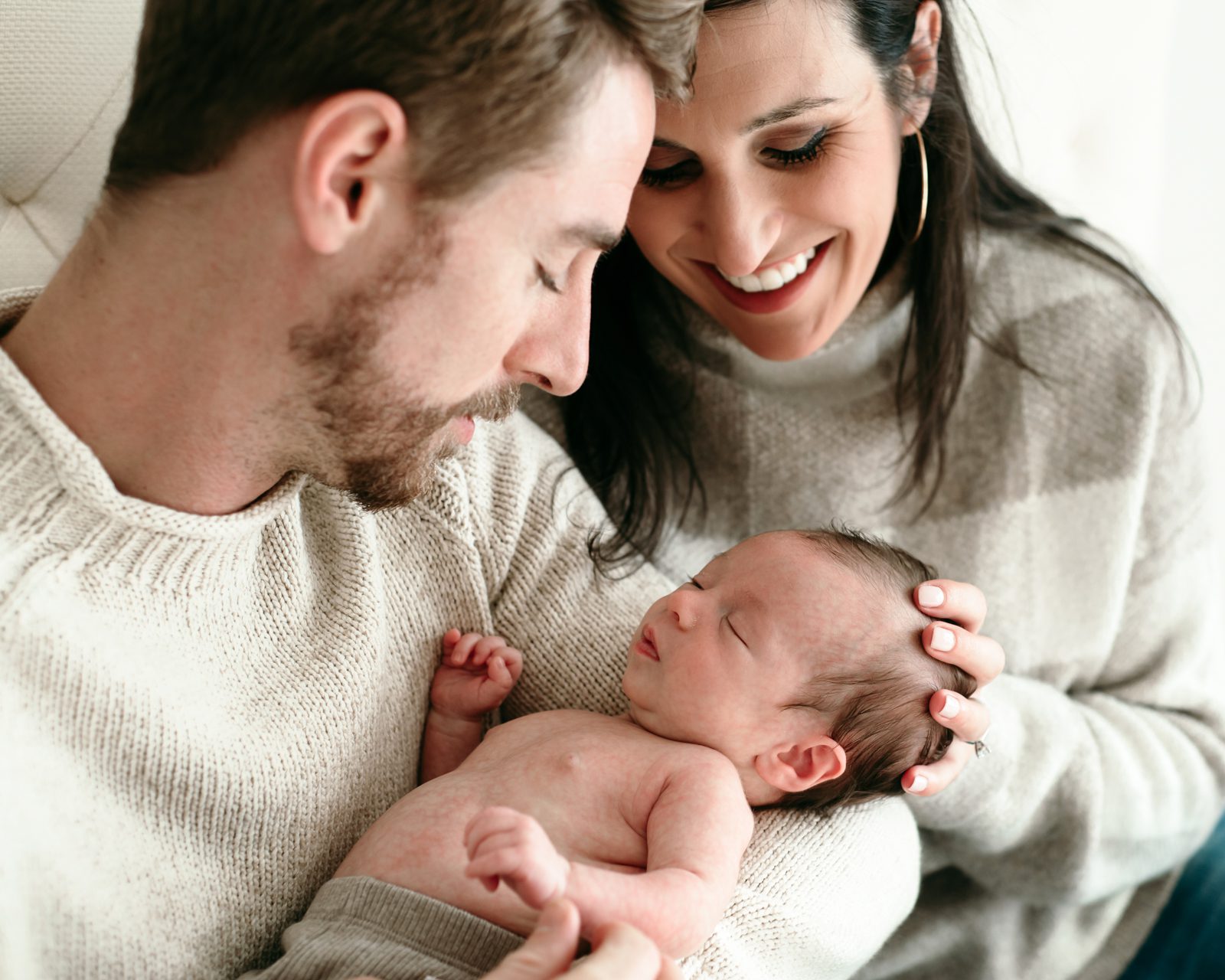 new parents holding their newborn baby boy and smiling down at him during a lifestyle newborn photoshoot