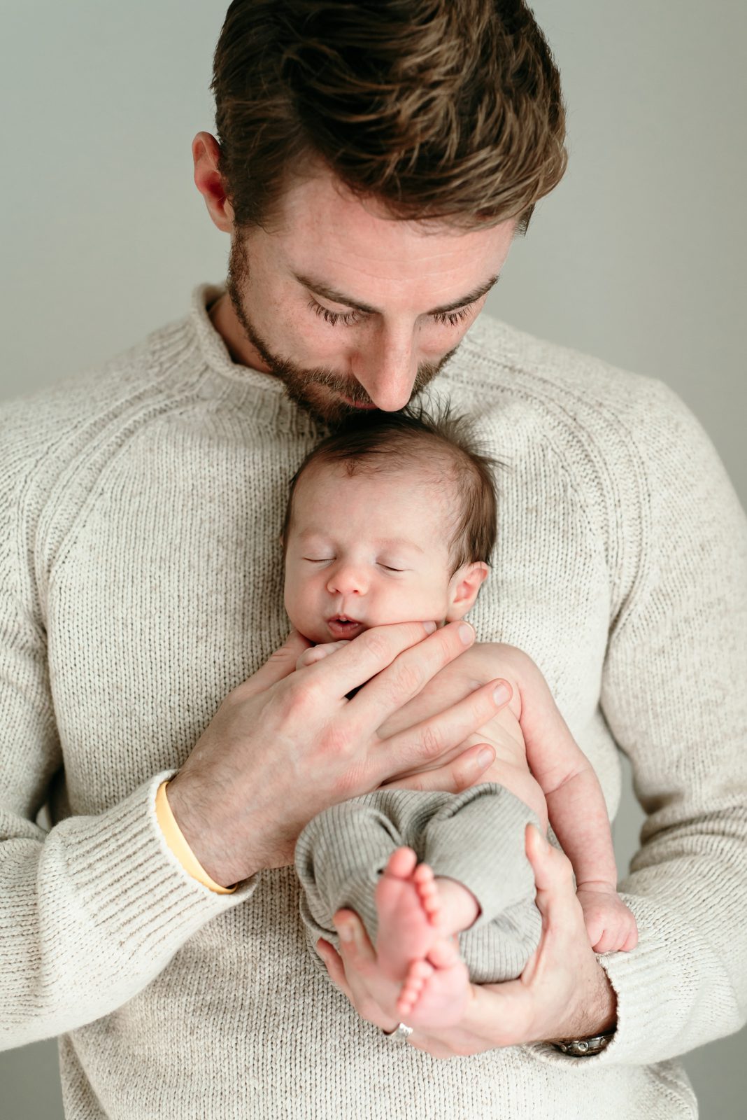 a new father holding his baby boy against his chest and resting his chin on the baby's head during an in home newborn photo session