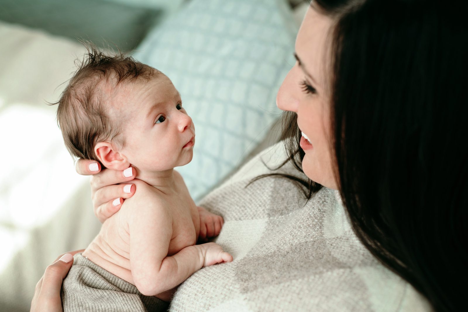 a mom and her baby boy looking at each other while they snuggle together on a bed during a natural light newborn photo session