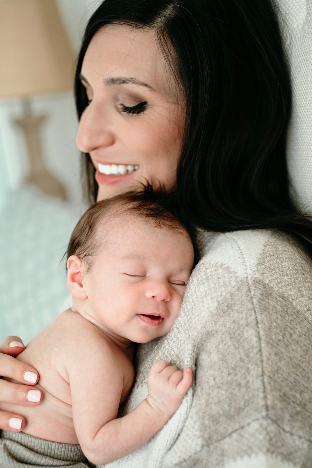 a mom cradling her baby boy against her chest and smiling during an in home natural light newborn photo session
