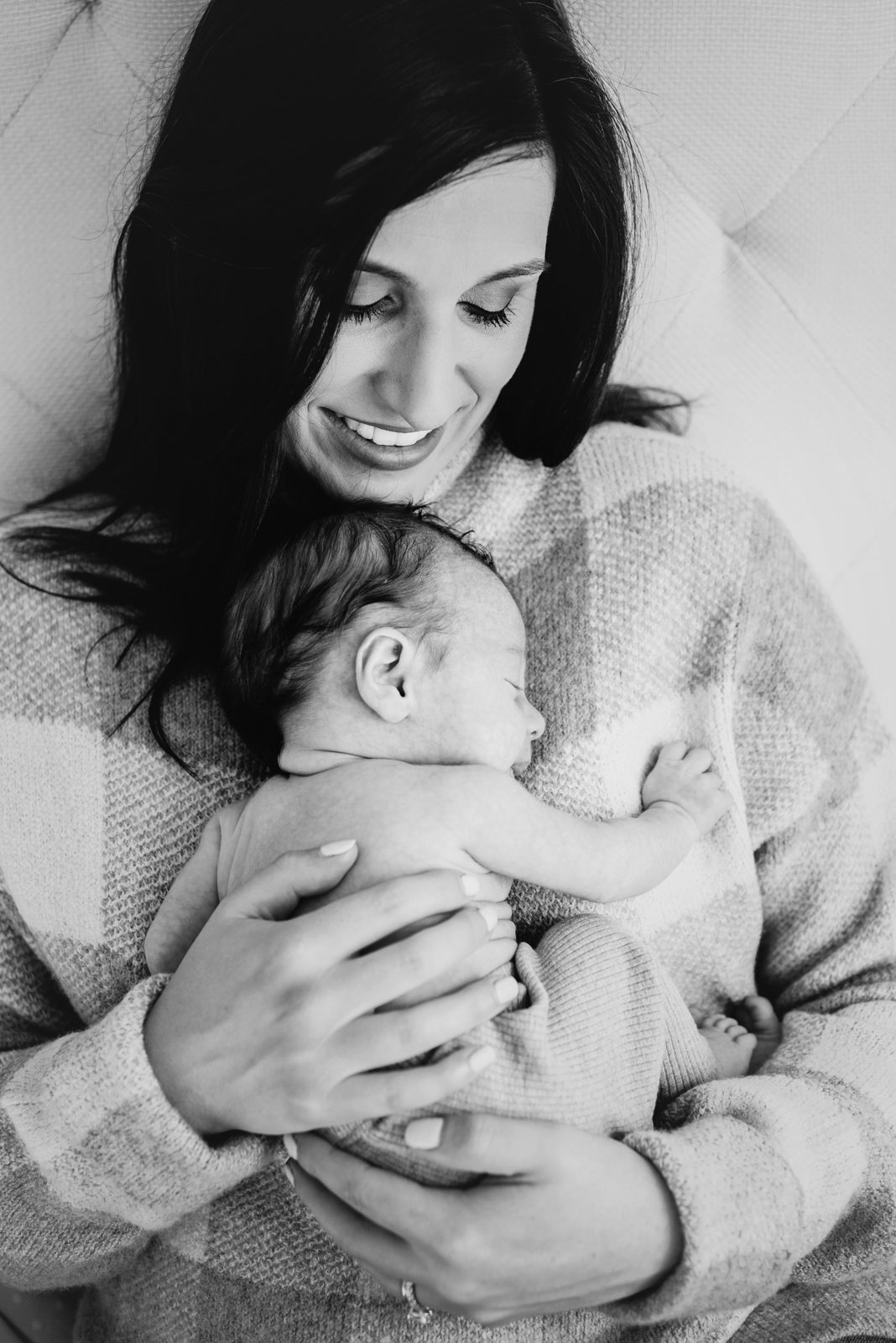 a black and white picture of a mom cradling her baby boy against her chest and smiling down at him during a natural newborn photoshoot