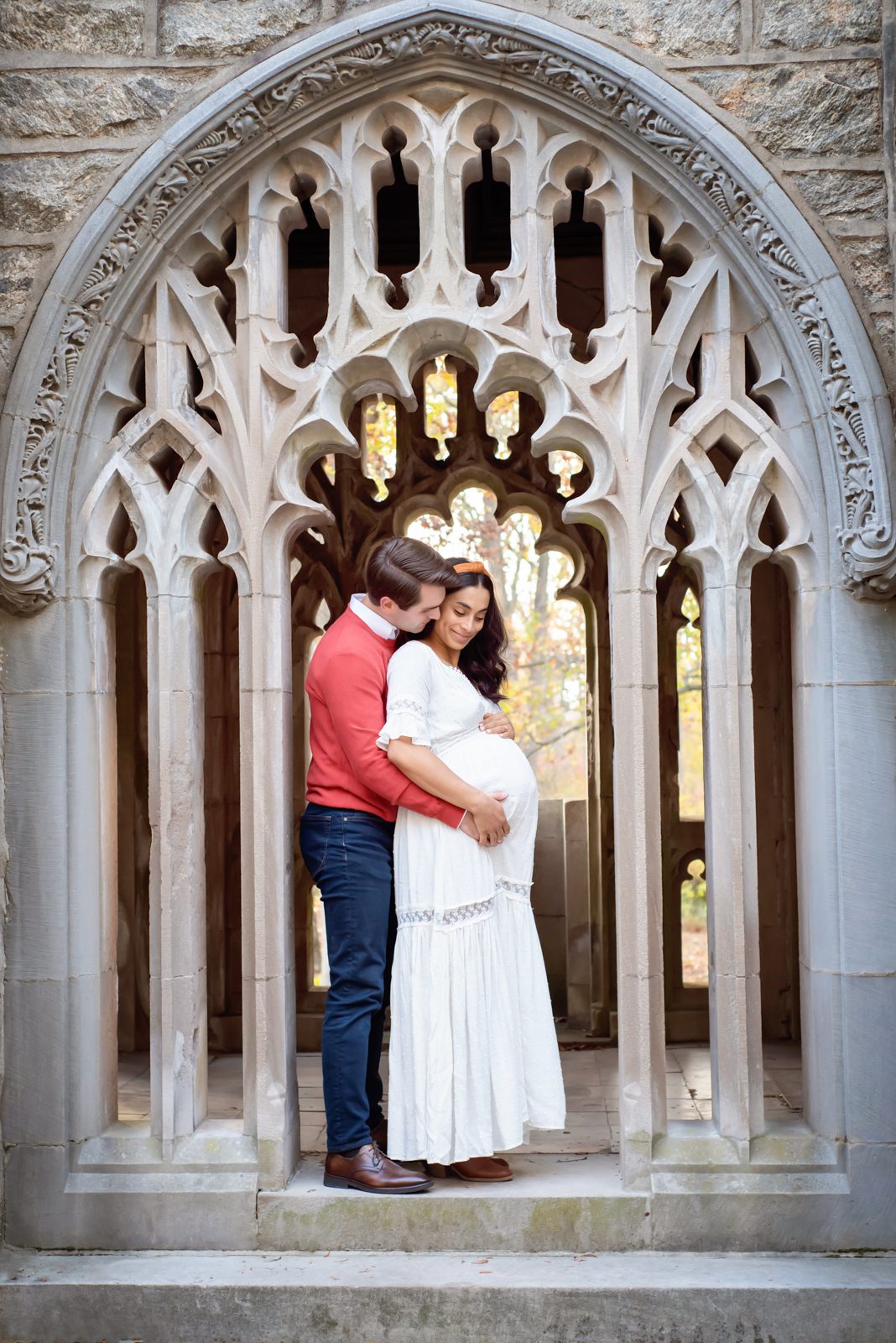 an expecting couple standing in a stone archway and cradling mom's belly during a valley forge maternity photoshoot