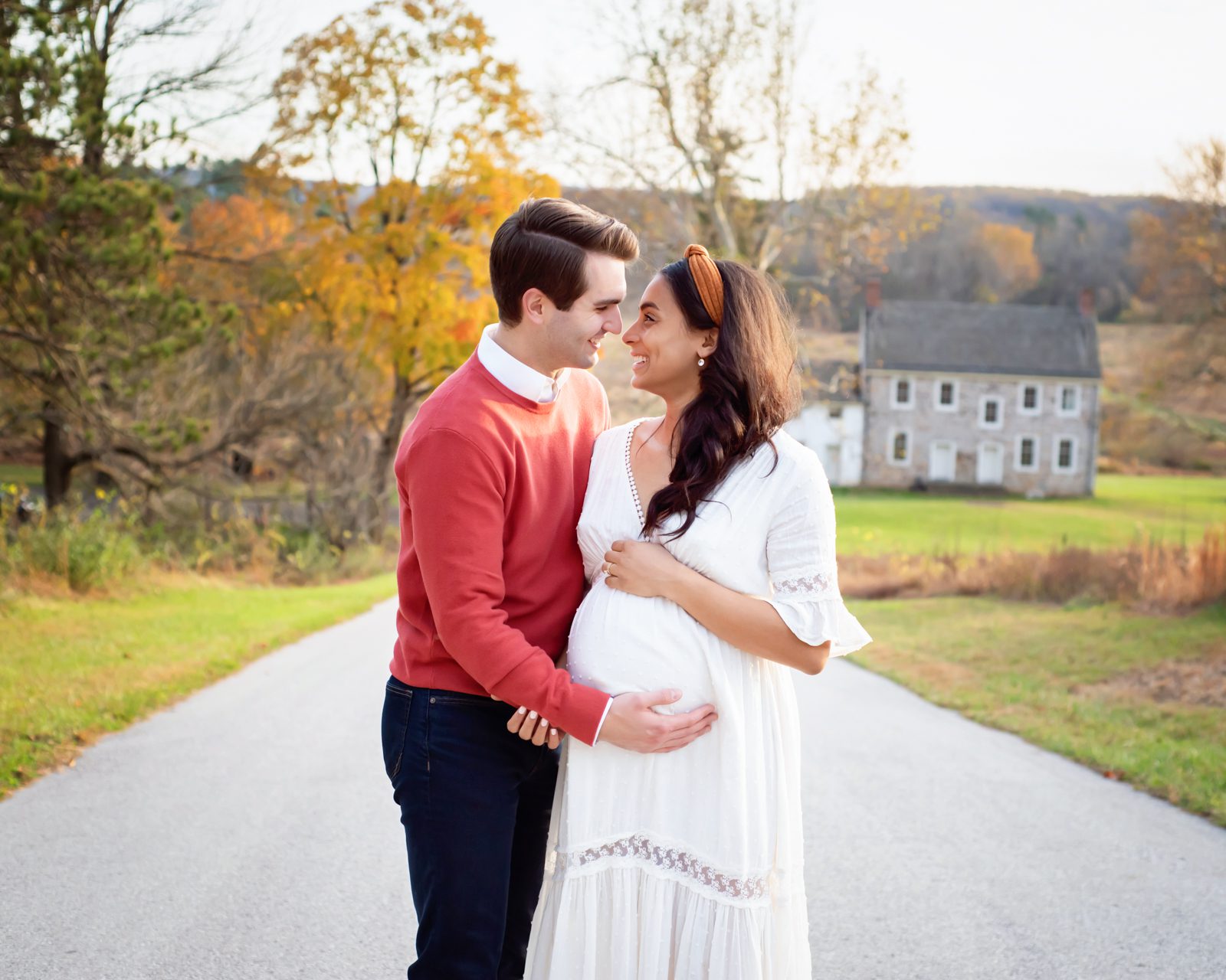 an expected couple standing on a path and looking at each other and laughing while they both cradle mom's belly during a Valley Forge maternity photo session