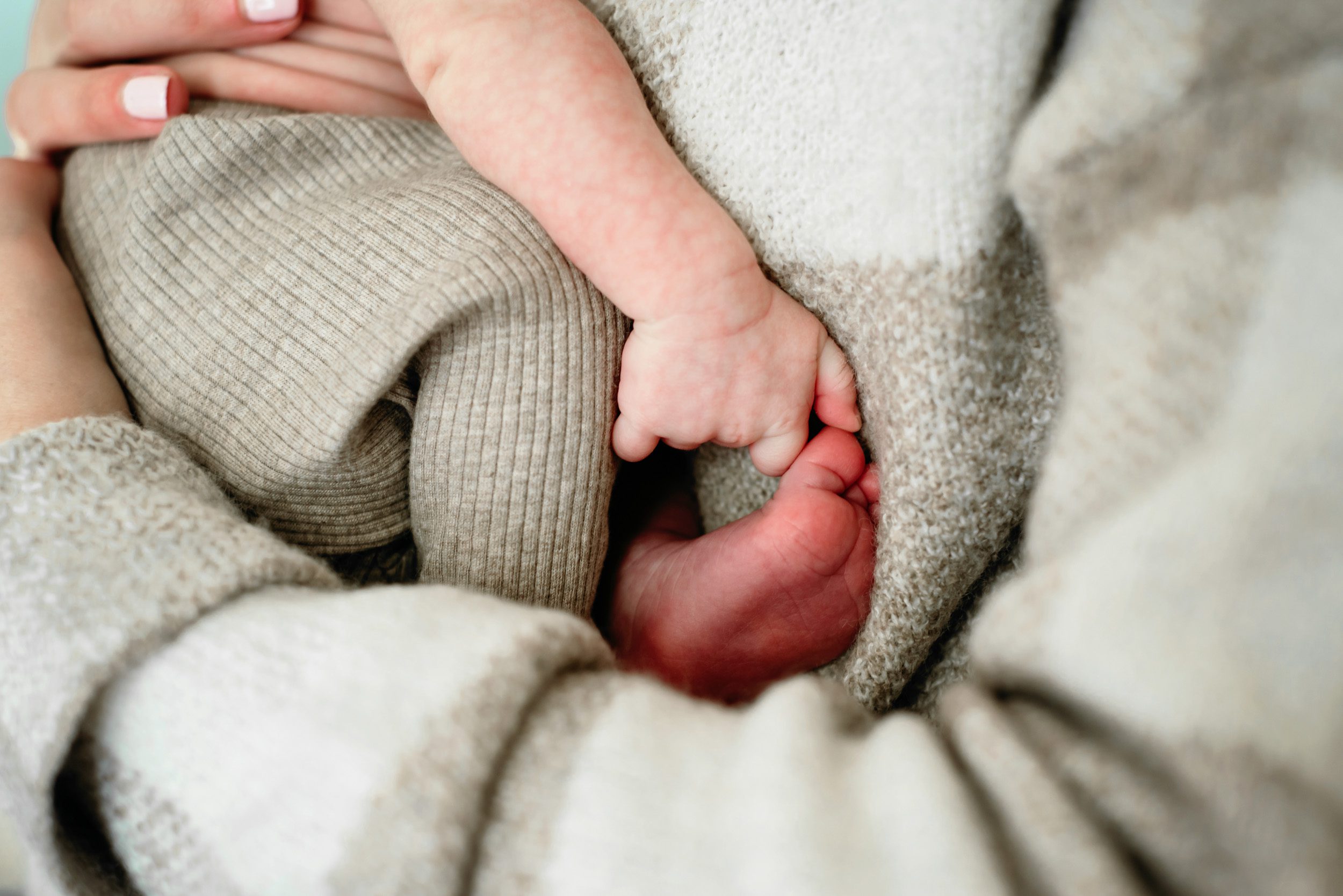 a close up picture of a baby boy grabbing his big toe with his thumb and forefinger while he snuggles up against his mother's chest during an in home newborn photo session