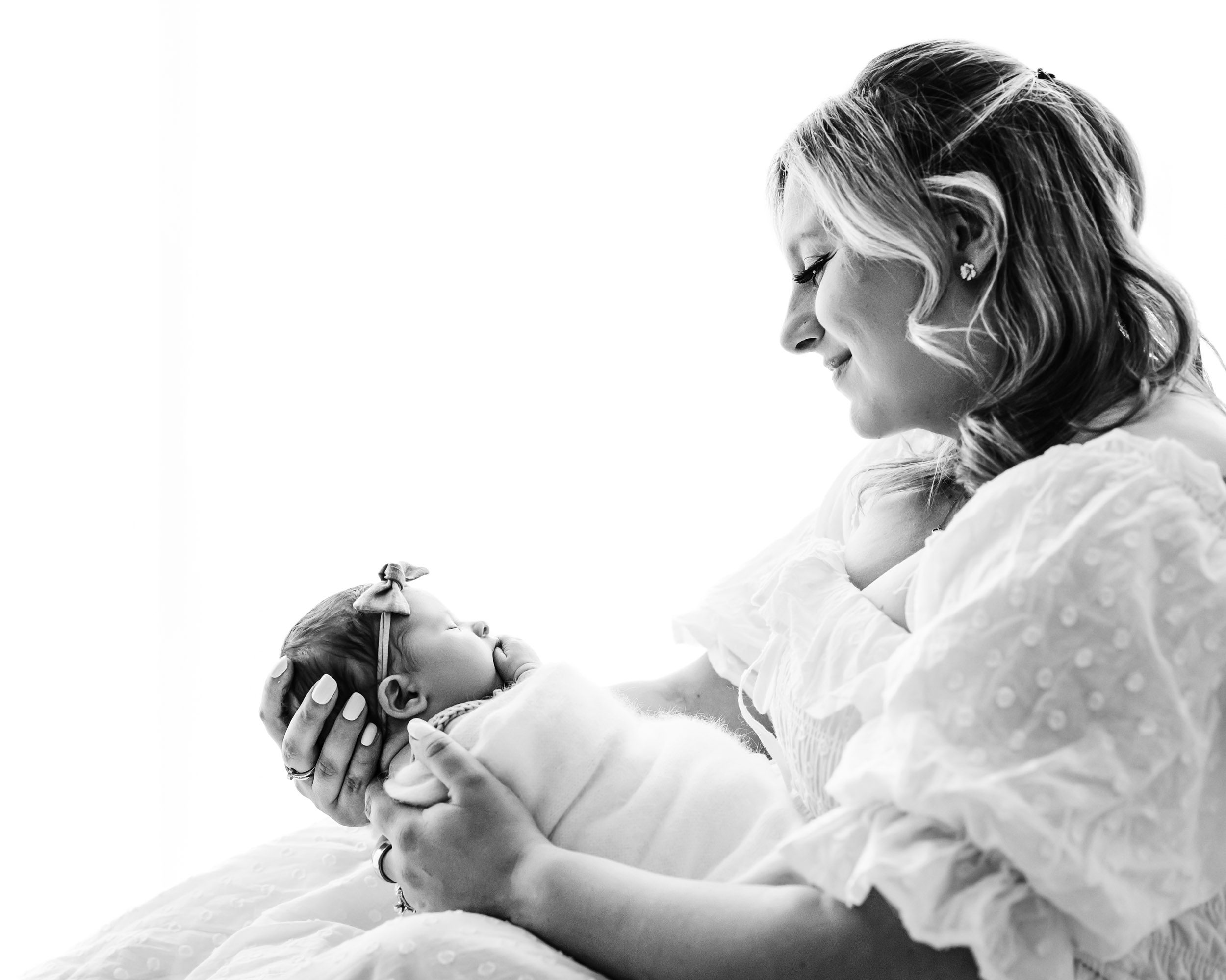 a black and white backlit photo of a new mom sitting and holding her baby girl and smiling down at her during a natural newborn photography session