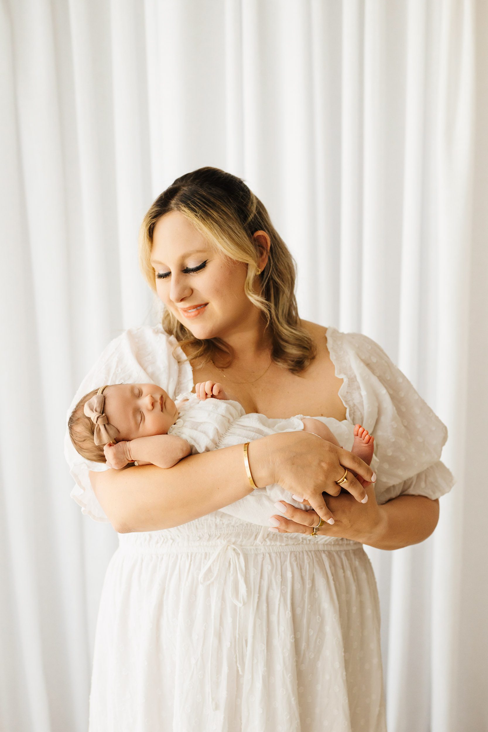 a new mom cradling her baby girl in her arms and smiling down at her during a natural newborn photography session