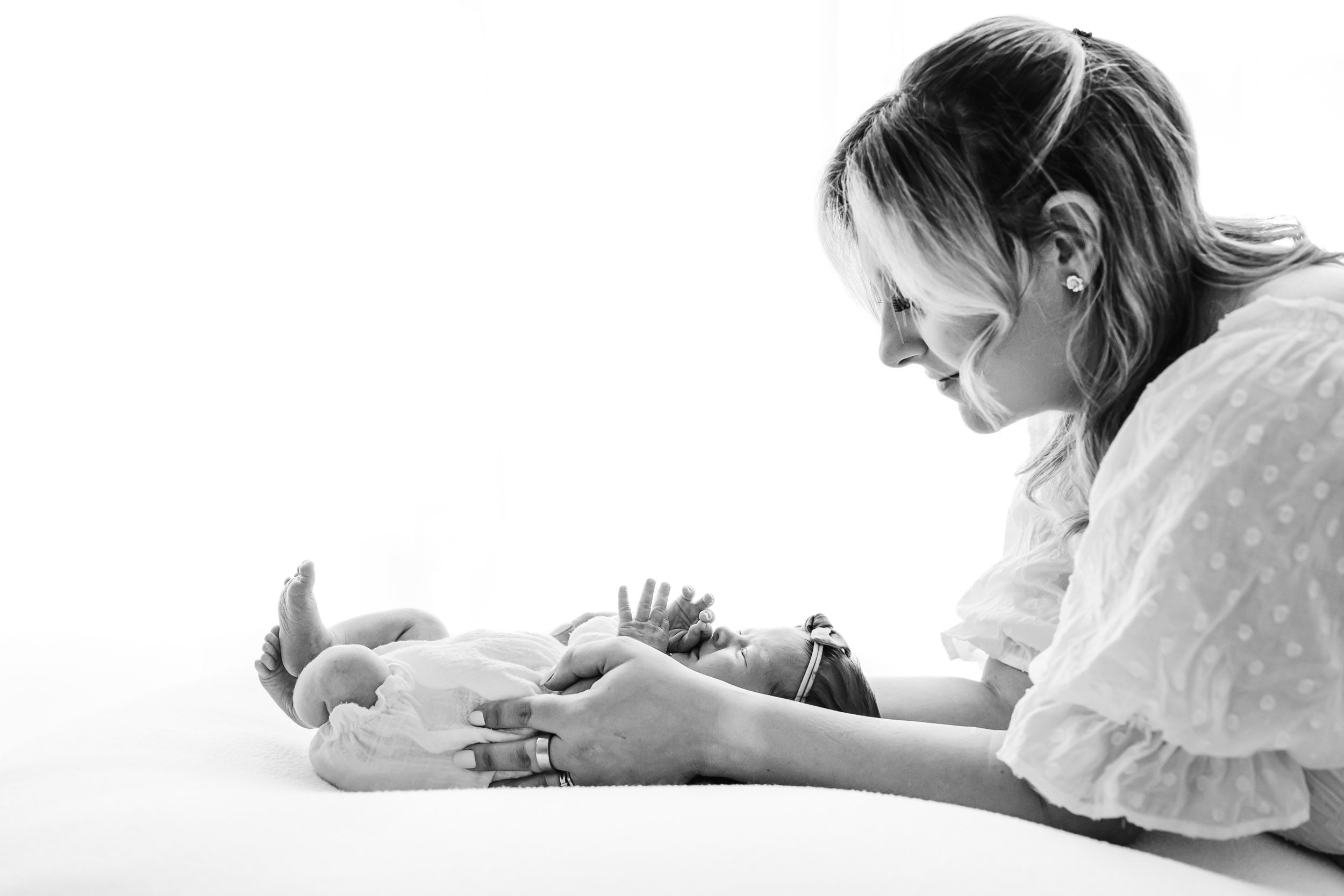 a black and white backlit photo of a baby girl laying on a beanbag as her mom smiles down at her during a natural newborn photography session