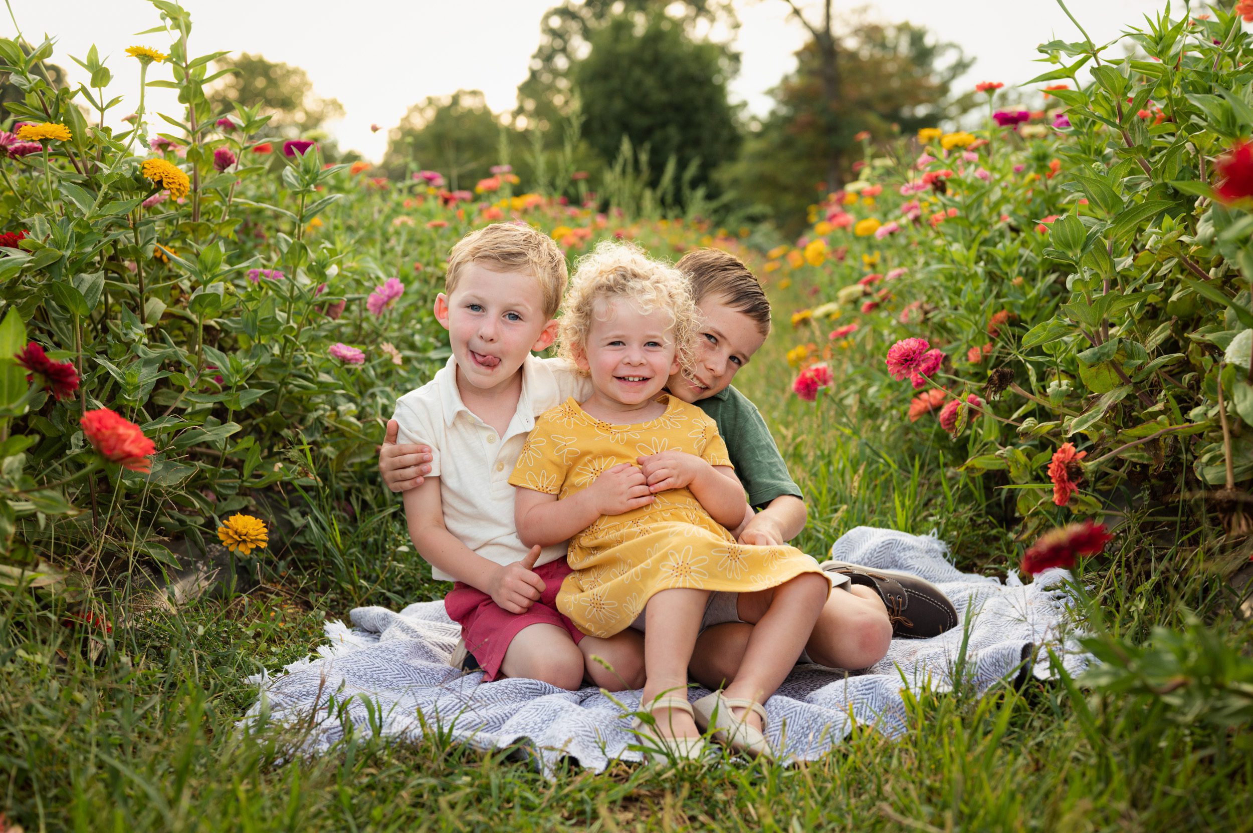 a little girl sitting on her two big brothers laps in a field of colorful flowers during a philadelphia family photoshoot