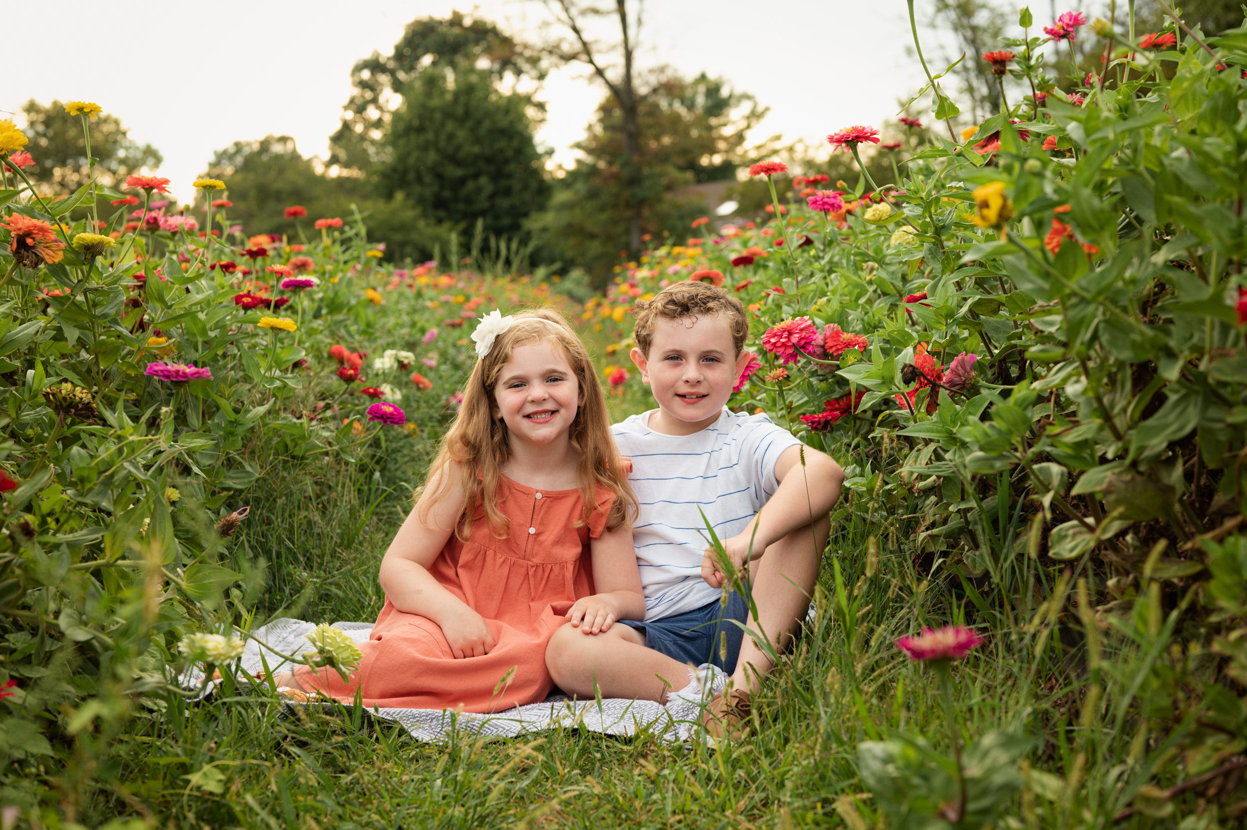 two siblings sitting in a field of colorful flowers and smiling at the camera during a philadelphia family photo session