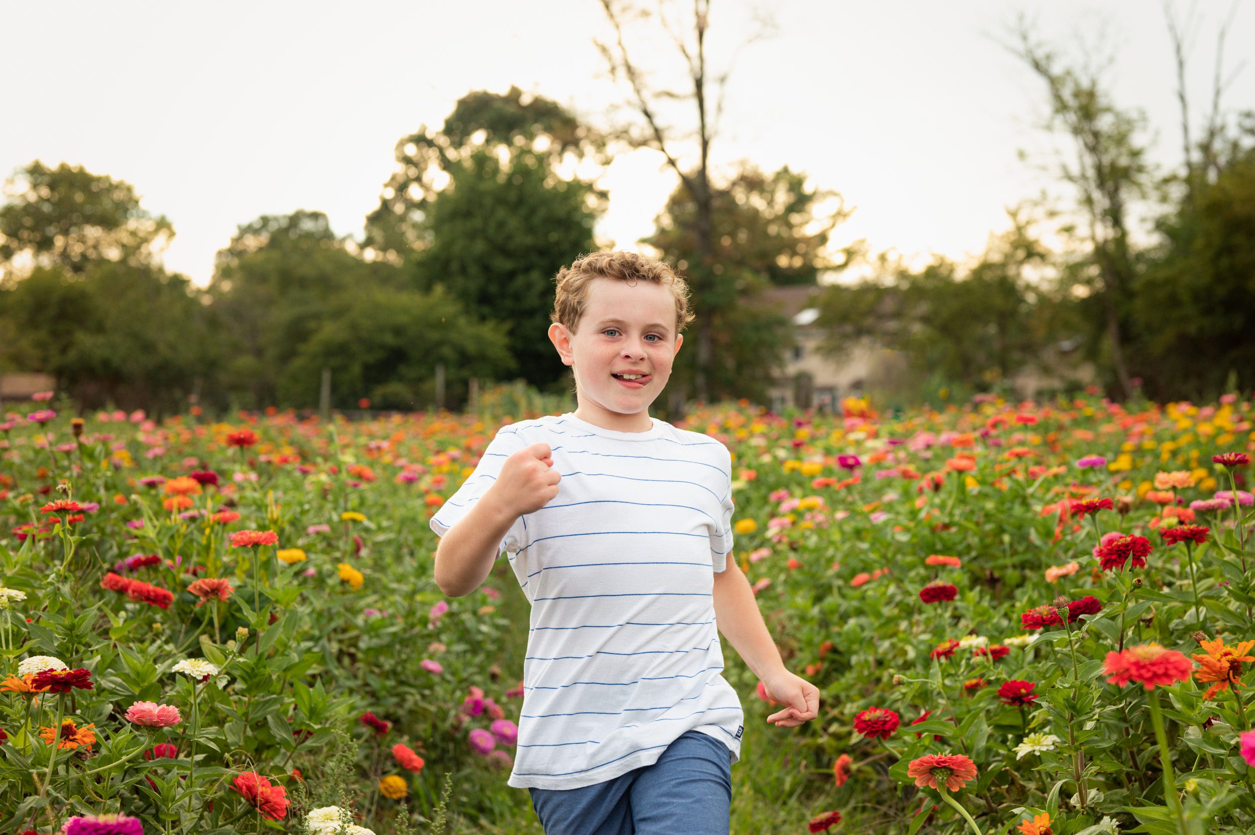 a young boy running through a field of colorful flowers and sticking her tongue out at the camera during a philadelphia family photo shoot